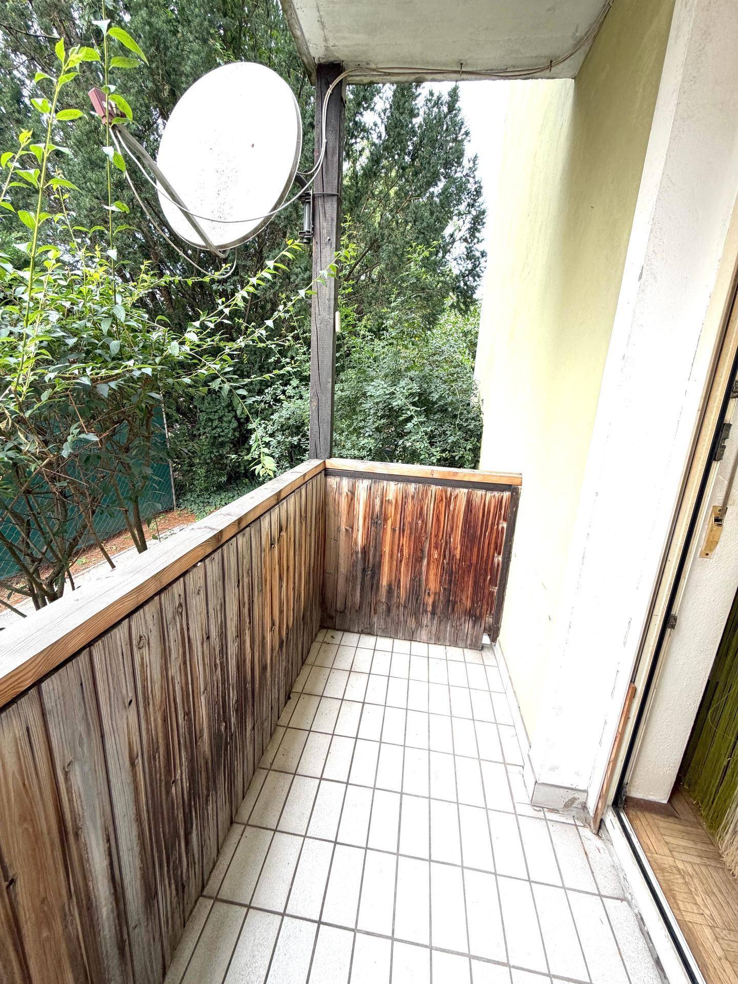 Kleiner Balkon mit Fliesenboden und Holzgeländer, umgeben von viel Grün.