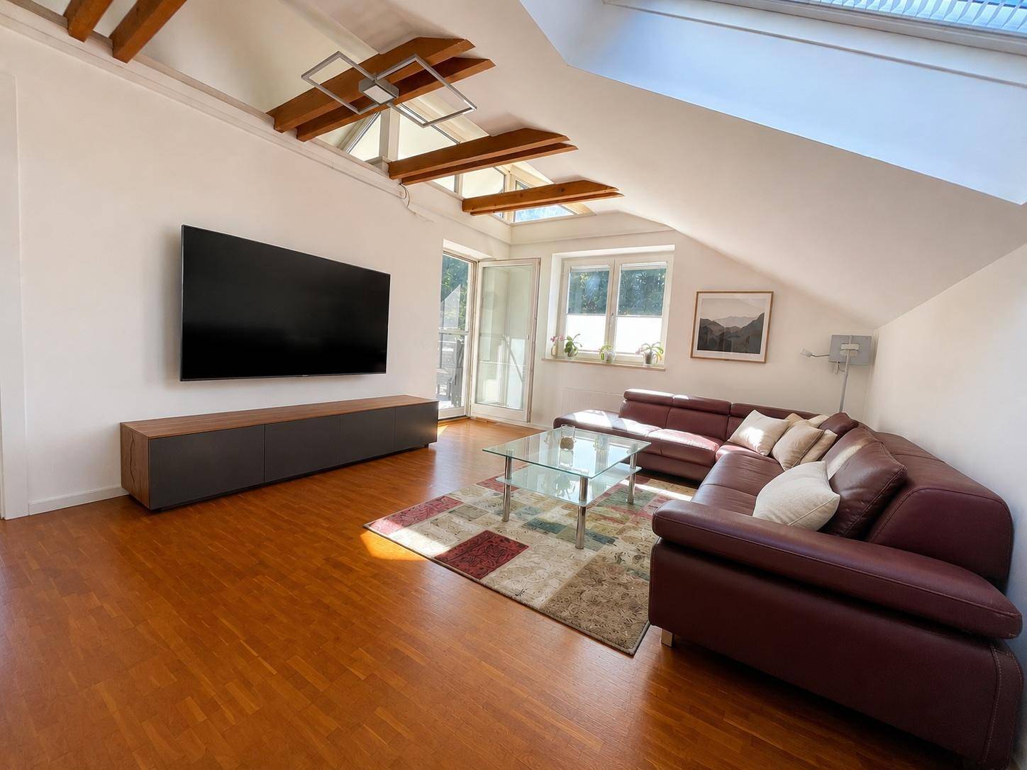 Gemütliches Wohnzimmer mit großem Fernseher, Ledersofa, Holzboden und mehreren Dachfenstern.