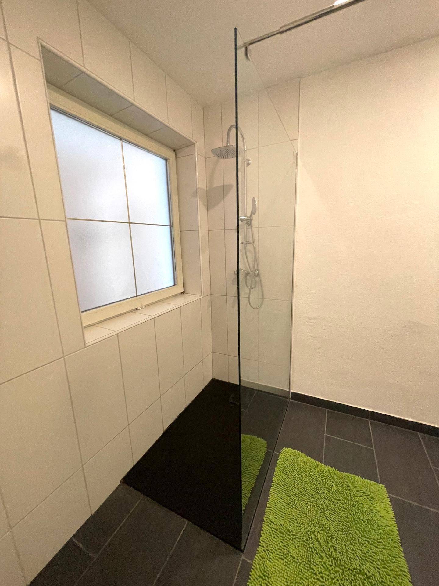 Ein moderner Duschbereich mit Glasabtrennung und dunklen Bodenfliesen.