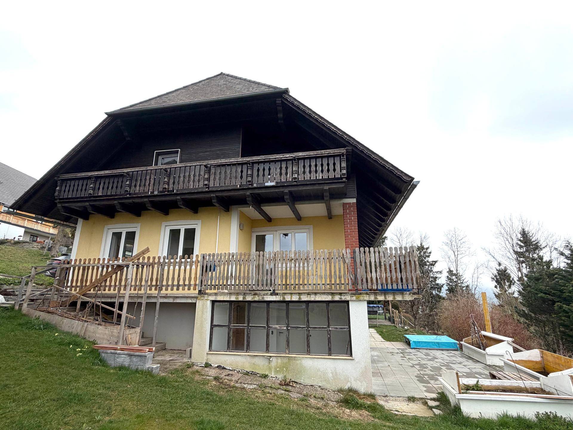 Charmantes Haus mit gelber Fassade, Holzbalkonen und einer großen Terrasse im Vordergrund.