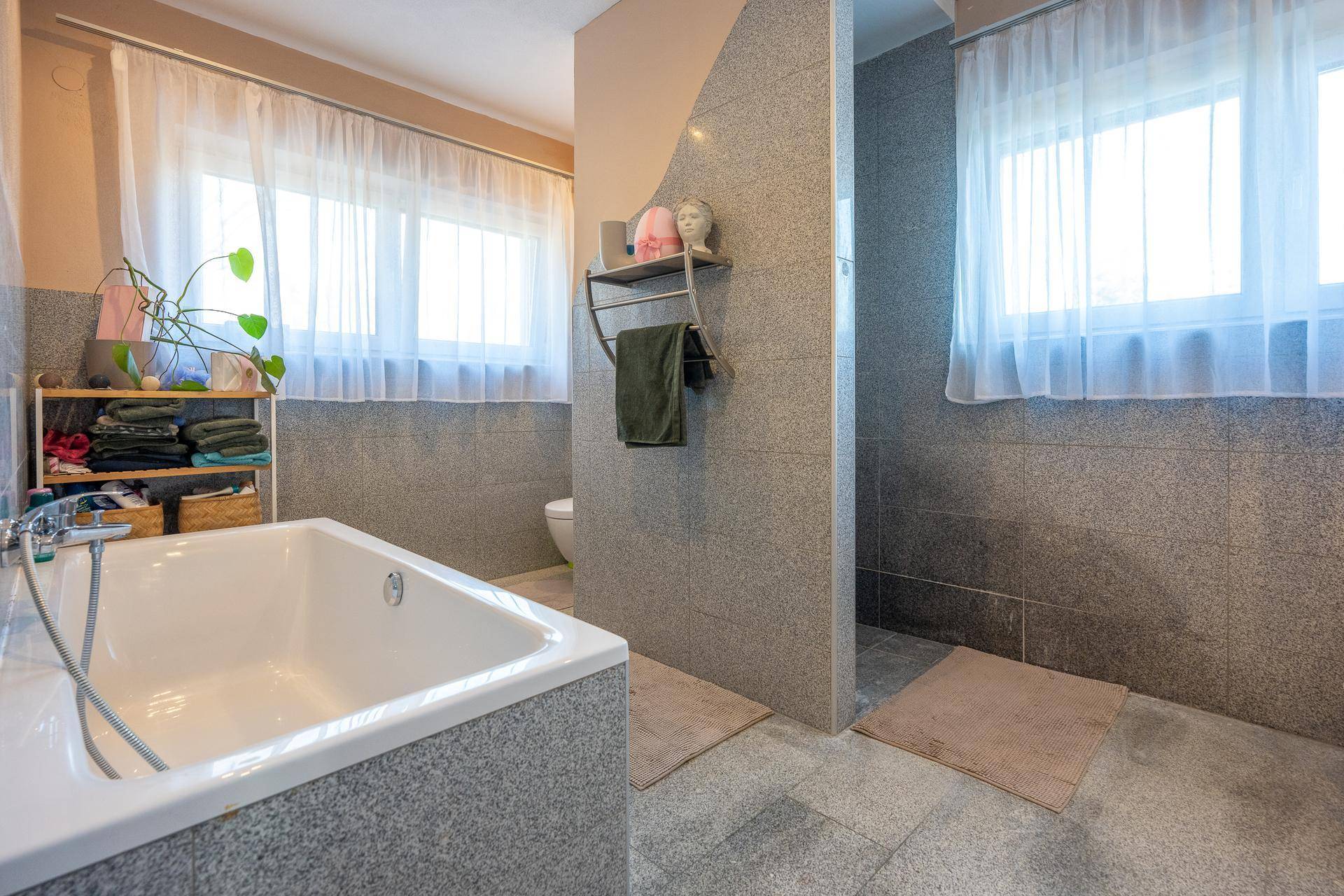 Geräumiges Badezimmer mit Badewanne, Dusche und zwei Fenstern für viel Tageslicht.