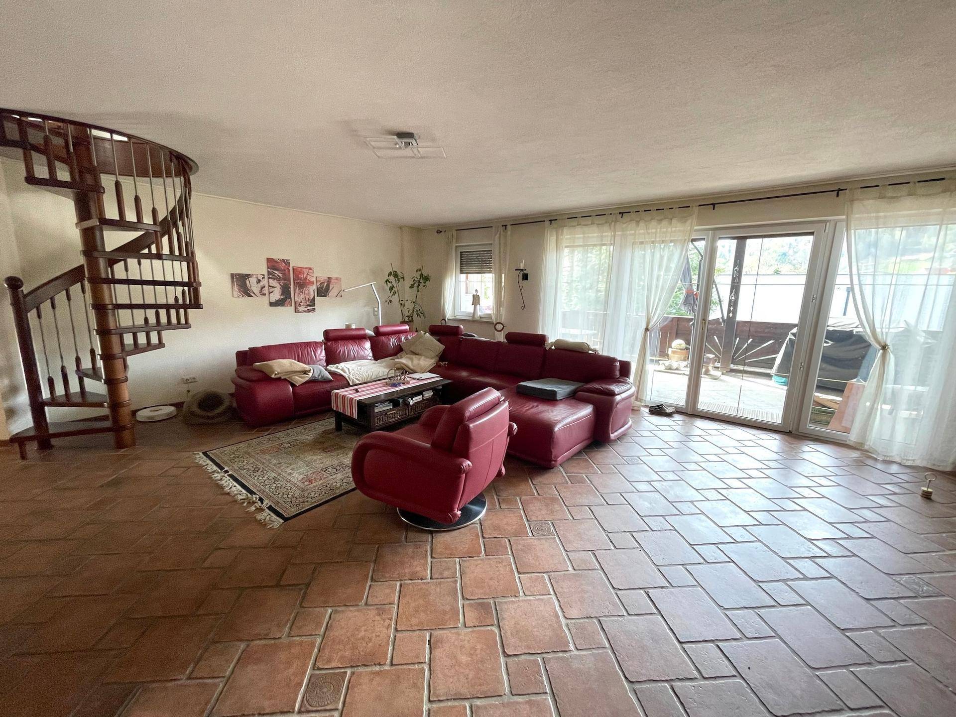 Ein Wohnzimmer mit Wendeltreppe, roter Ledercouch und Terrakottaboden.