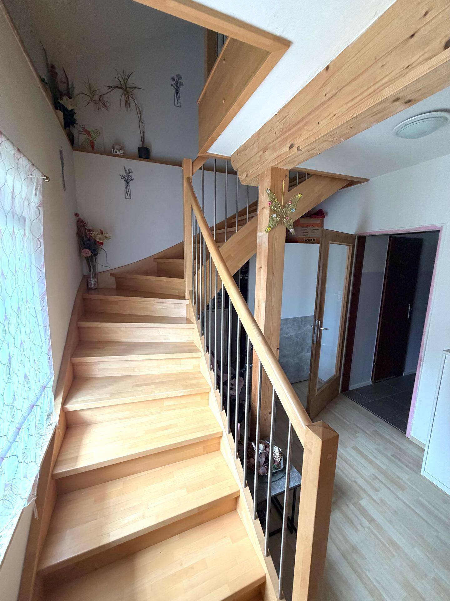 Holztreppe mit Metallgeländer führt in die obere Etage, umgeben von hellen Wänden und Laminatboden.
