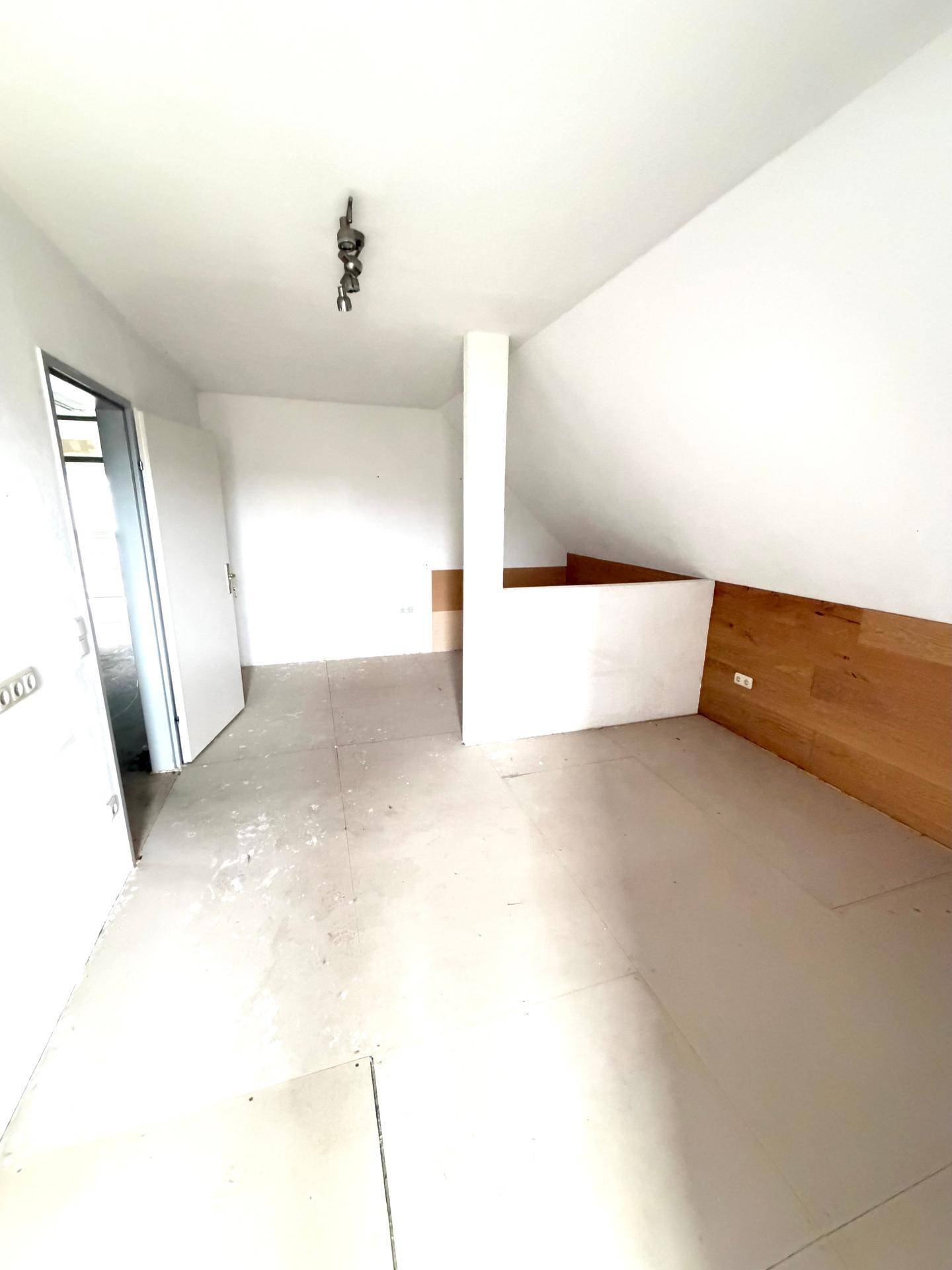 Helles Dachgeschosszimmer mit schrägen Wänden und Holzakzenten, bereit für den Ausbau.