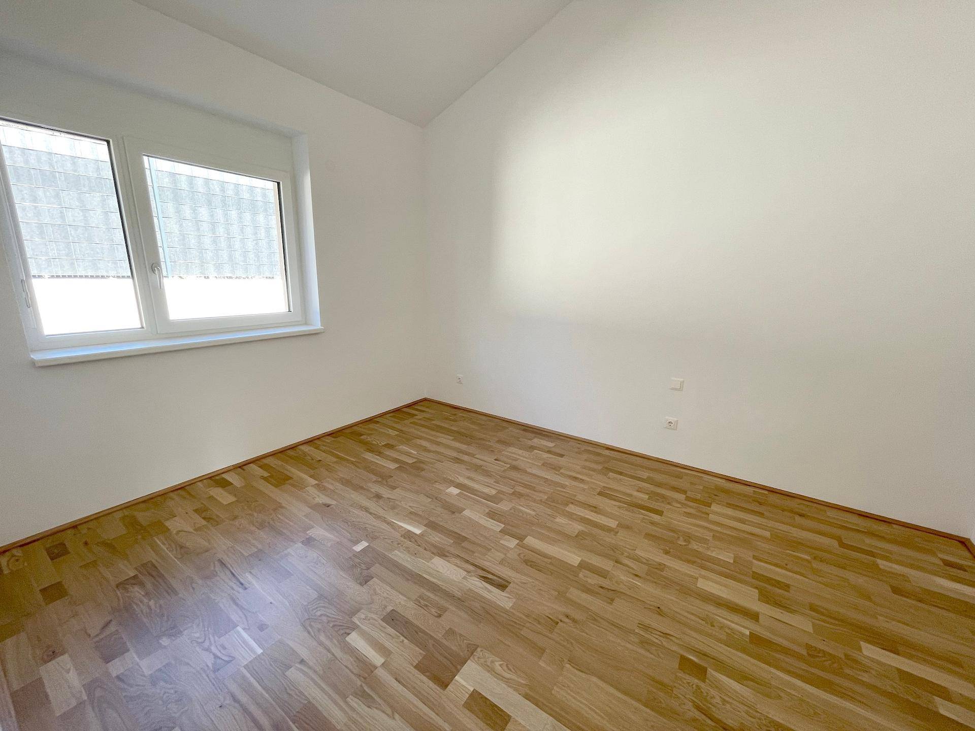 Leeres Zimmer mit Holzboden und großem Fenster, ideal als Schlaf- oder Kinderzimmer.
