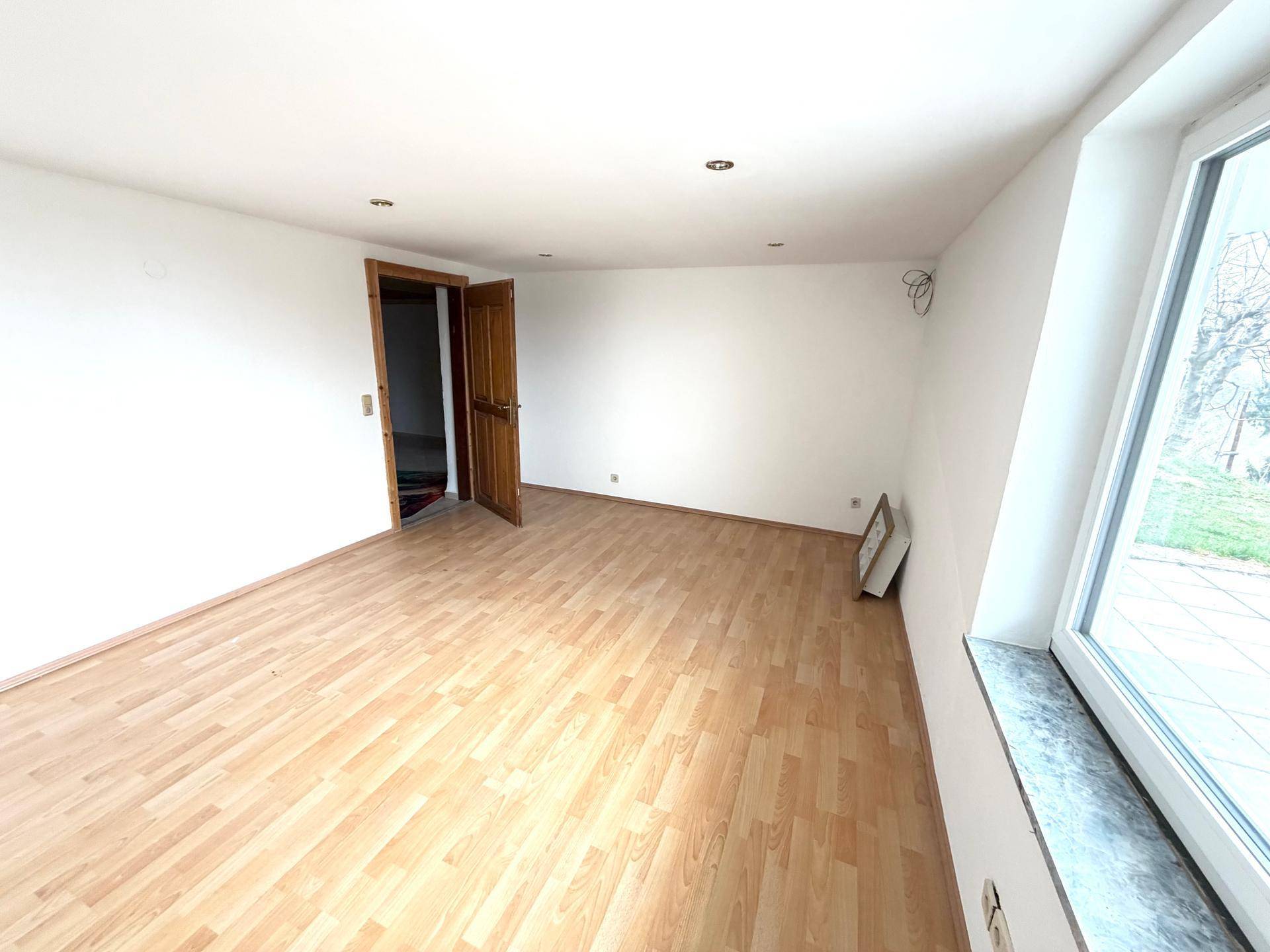 Freundliches Zimmer mit Holzboden, weißen Wänden und viel Tageslicht, bietet eine angenehme Atmosphäre.