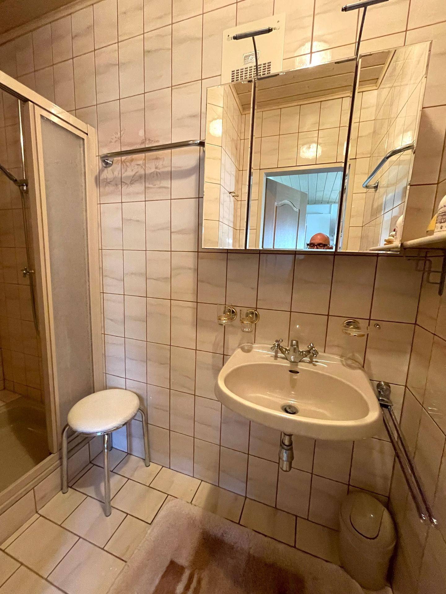 Ein Badezimmer mit hellen Fliesen, Waschbecken, Spiegelschrank und Duschkabine.