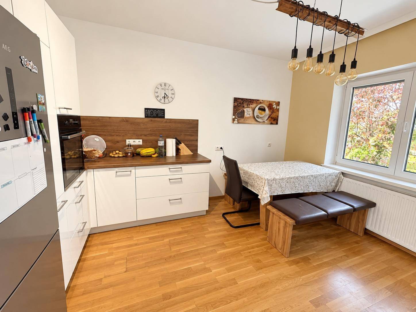 Moderne Wohnküche mit hellem Holzboden, Essbereich und integrierten, hochwertigen Geräten.