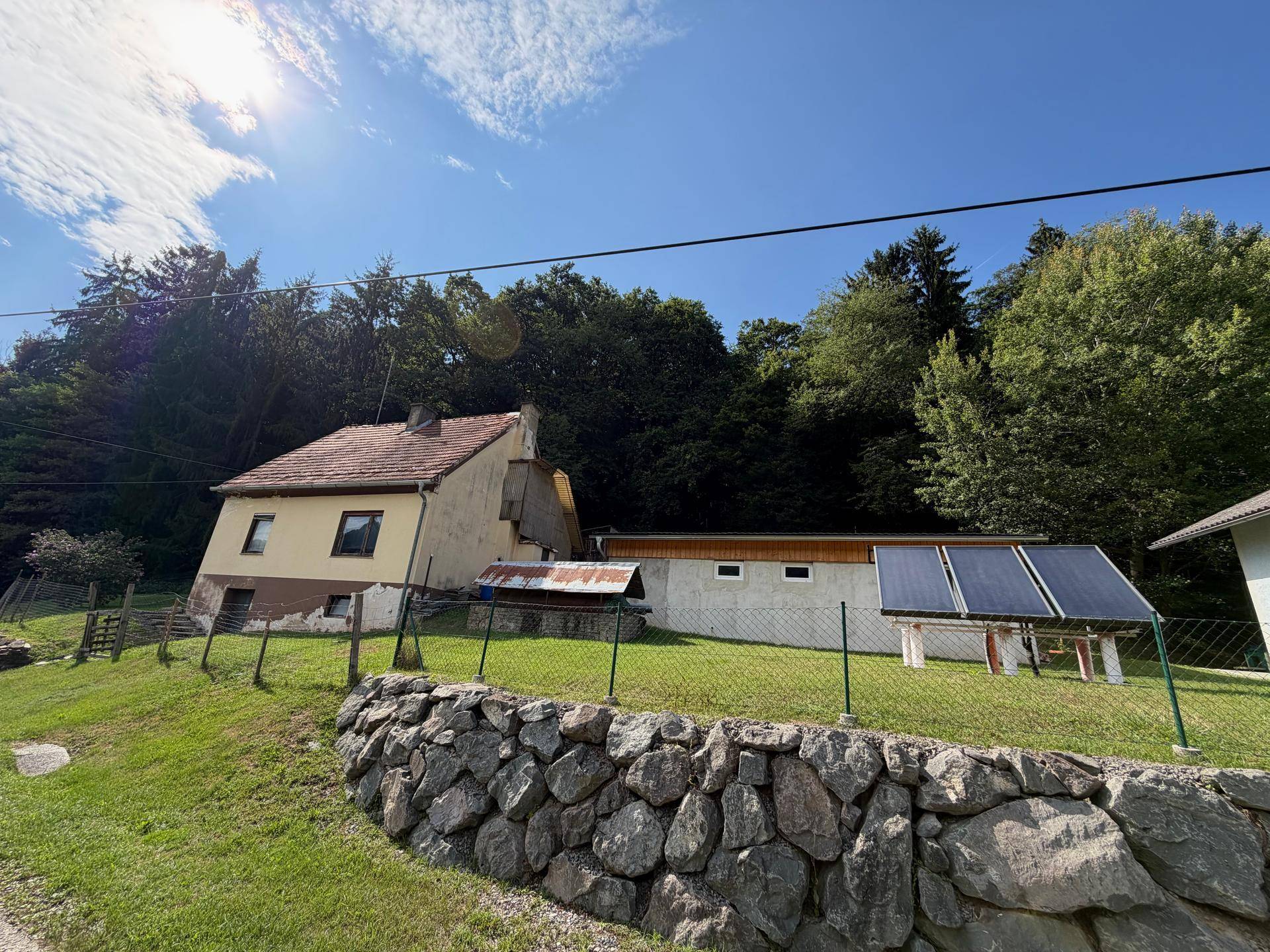 Ansicht des älteren Hauses und Nebengebäudes mit Solaranlage, umgeben von Feldern und Wald.
