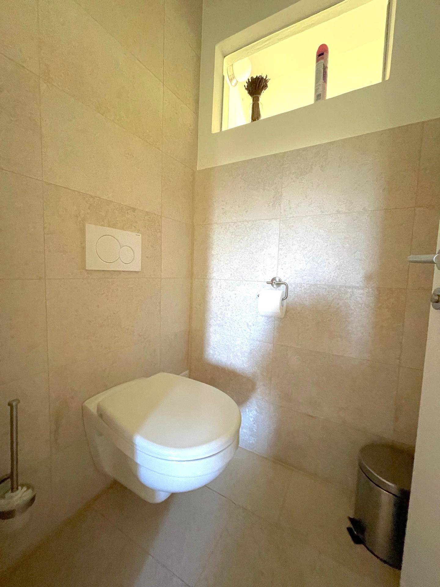 Modern gefliestes Gäste-WC mit wandhängendem WC und kleinem Fenster für Belüftung.