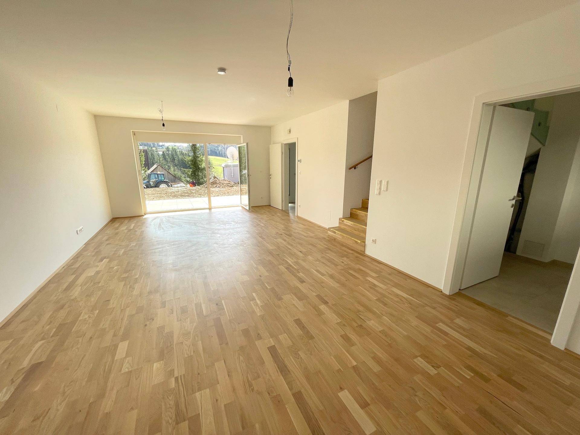 Heller, leerer Wohnbereich mit Holzboden und großer Schiebetür zum Außenbereich.