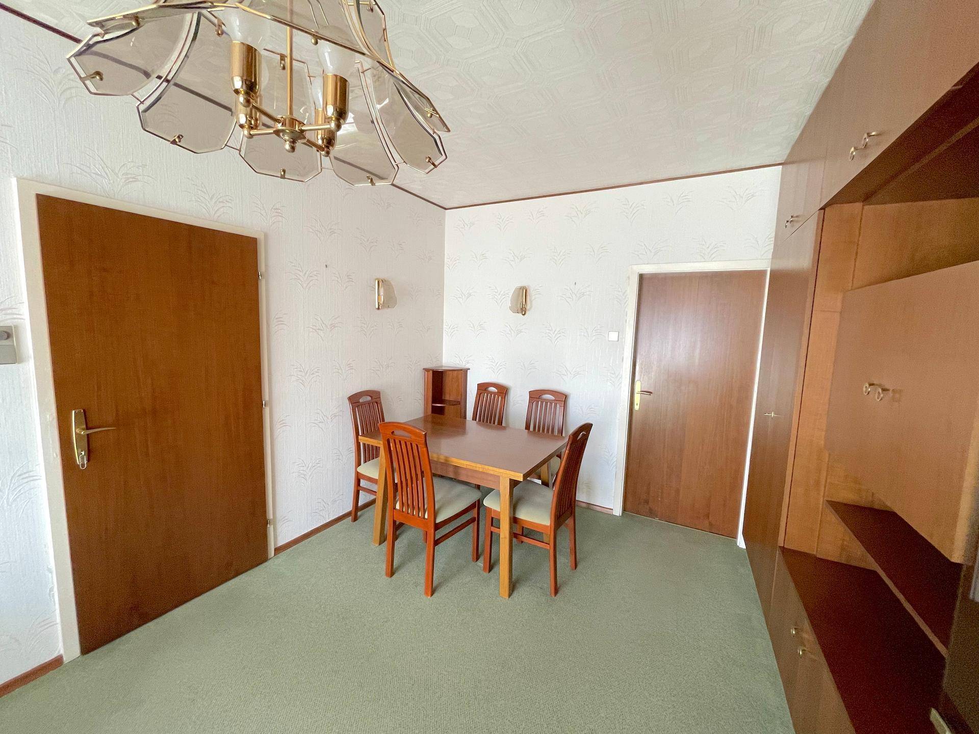 Essbereich mit Holztisch und Stühlen, umgeben von Schrankwänden und Teppichboden.