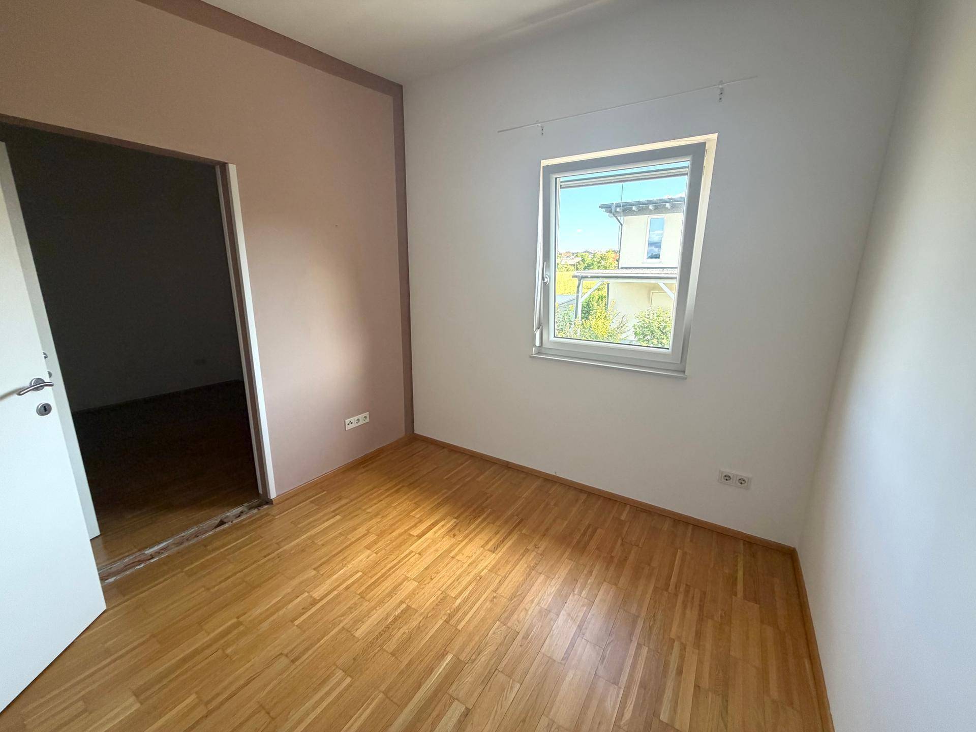 Unmöbliertes Zimmer mit Holzboden und Fenster mit Blick nach draußen.