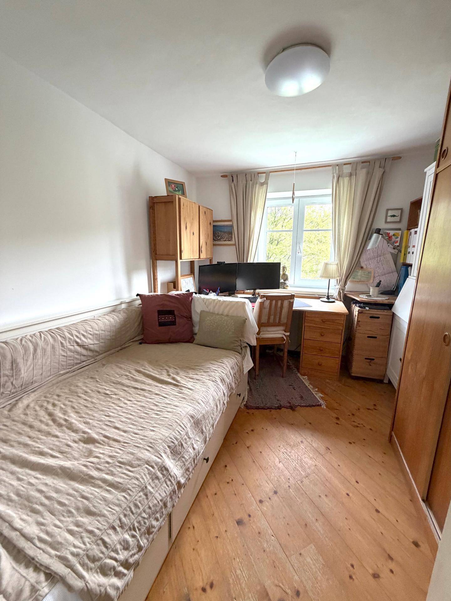 Gemütliches Schlafzimmer mit Holzboden, Einzelbett und Schreibtisch am Fenster.
