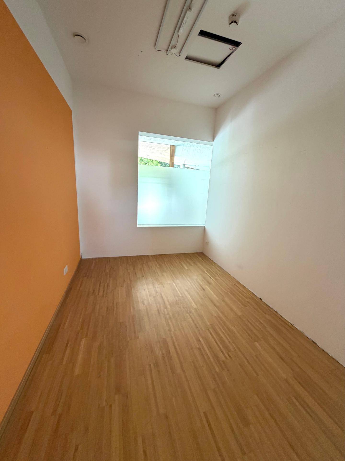 Helles Büro mit Holzfußboden, einer orangefarbenen Akzentwand und einem Fenster mit Sichtschutz.