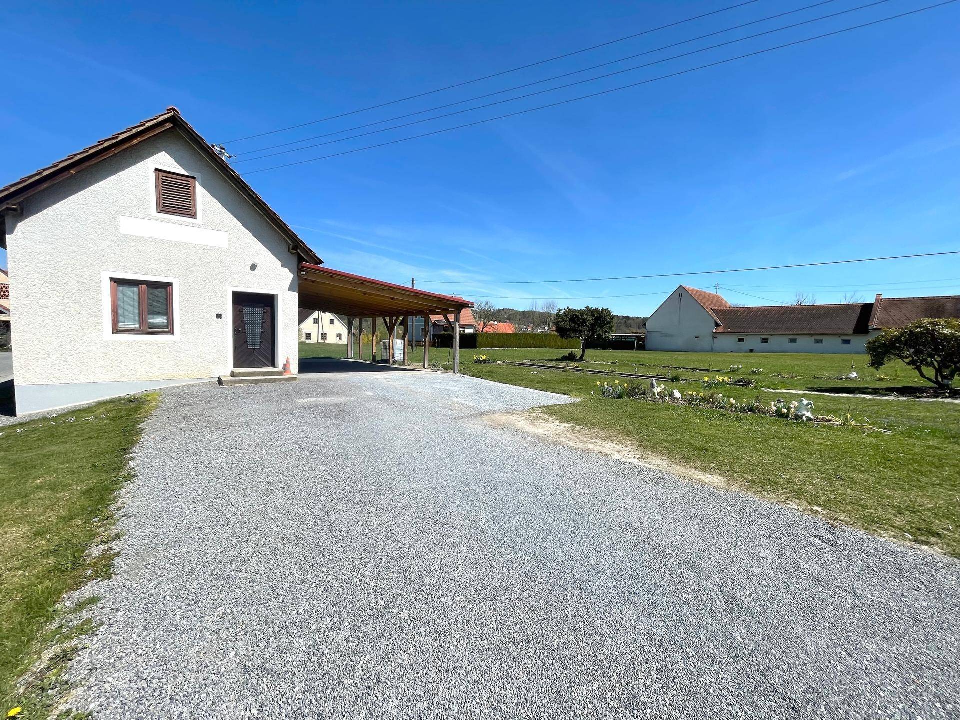 Außenansicht des Hauses mit Kiesauffahrt, Carport und großem Gartenbereich.