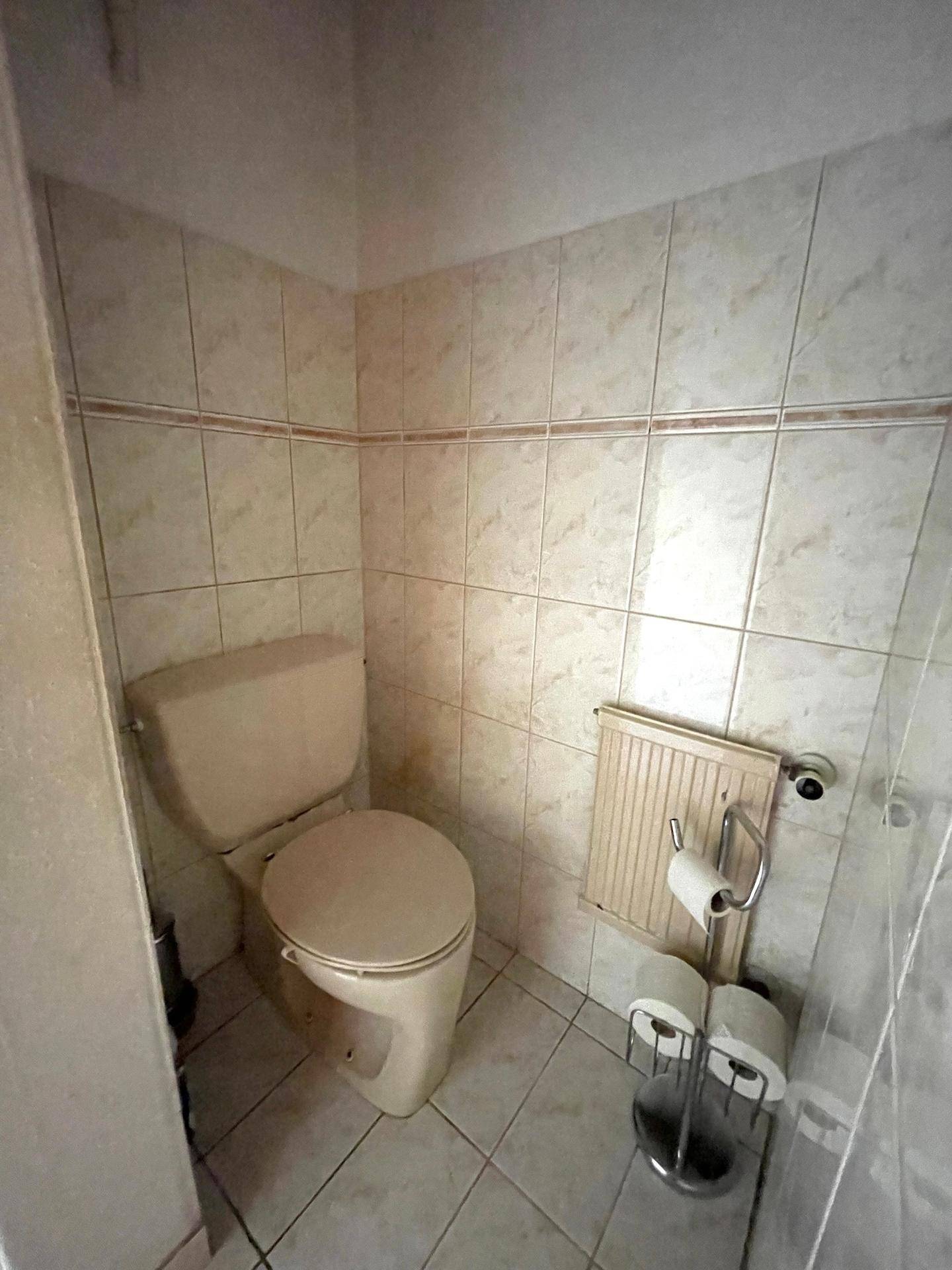 Kleines separates WC mit beigefarbenen Fliesen und einfacher Ausstattung.