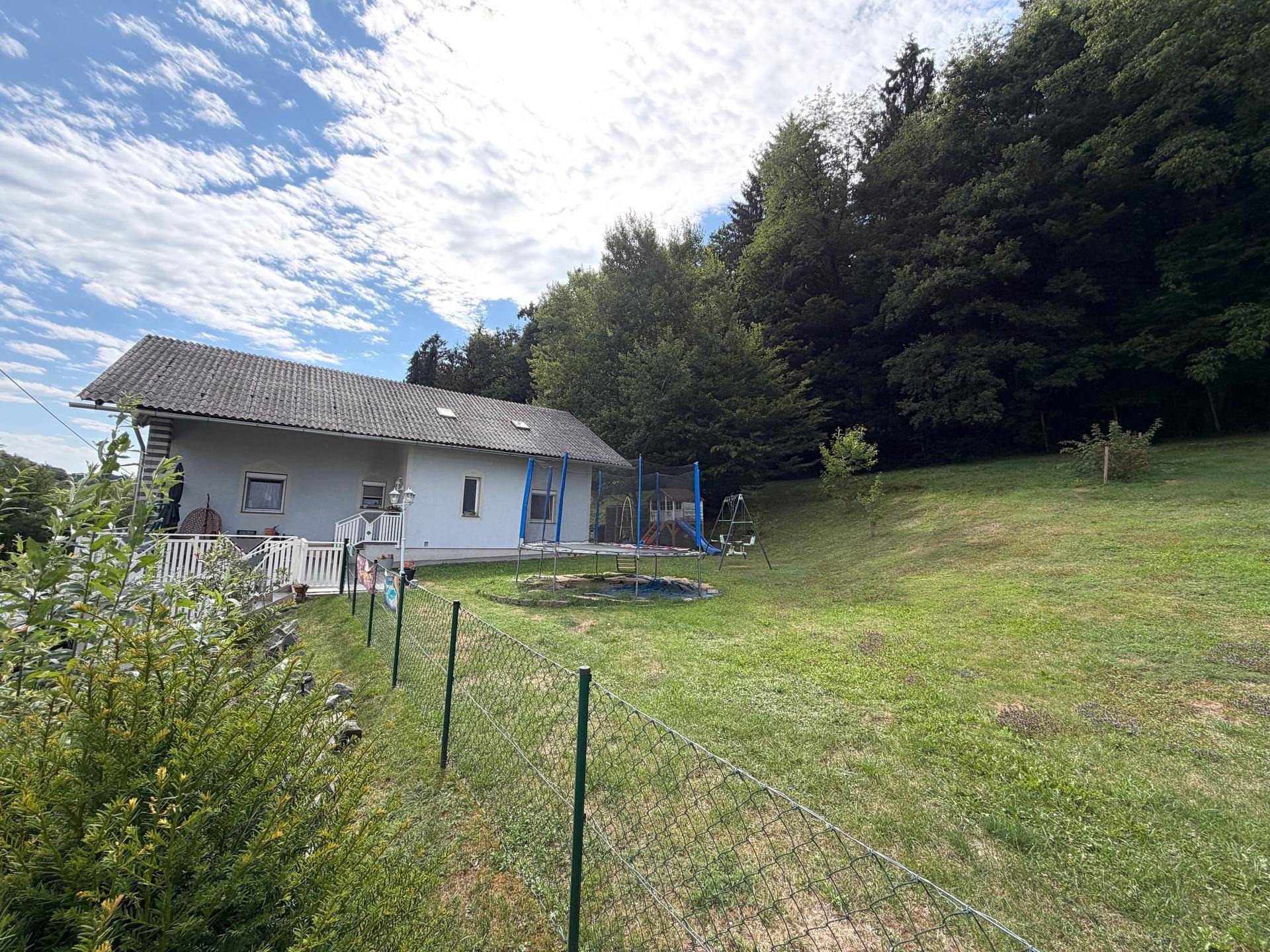 Weitläufiger Garten mit Rasenfläche, Trampolin und Blick auf das Haus und die umliegende Landschaft.