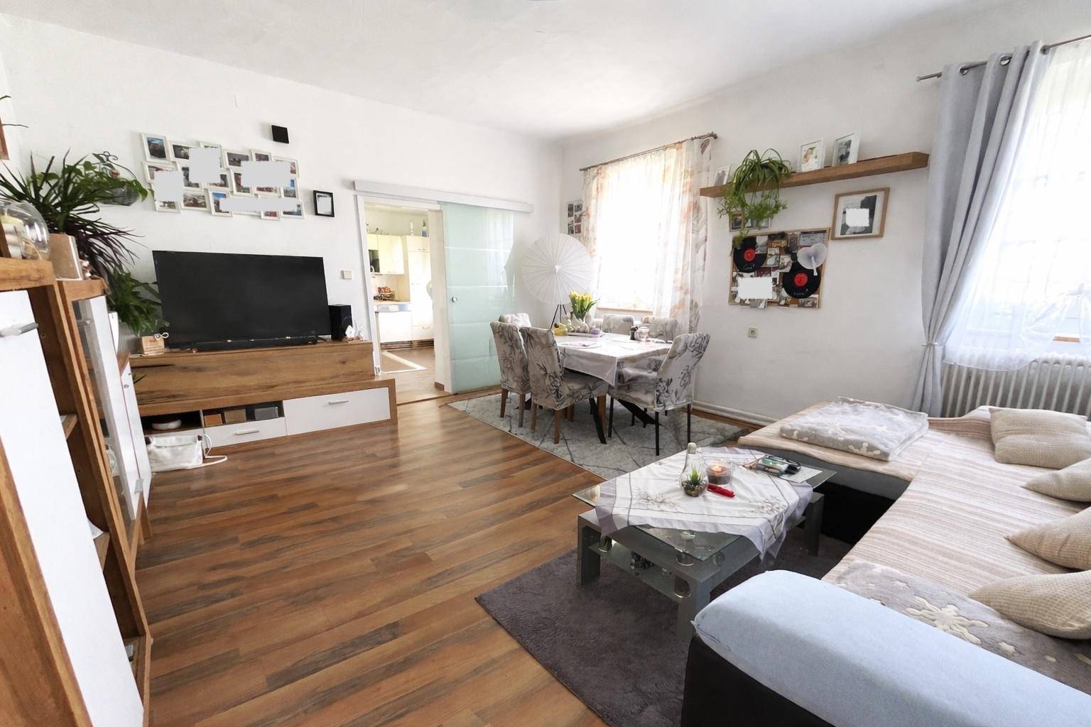 Moderner Wohnbereich mit Laminatboden, Fernseher, Sofa und Essbereich im Hintergrund.