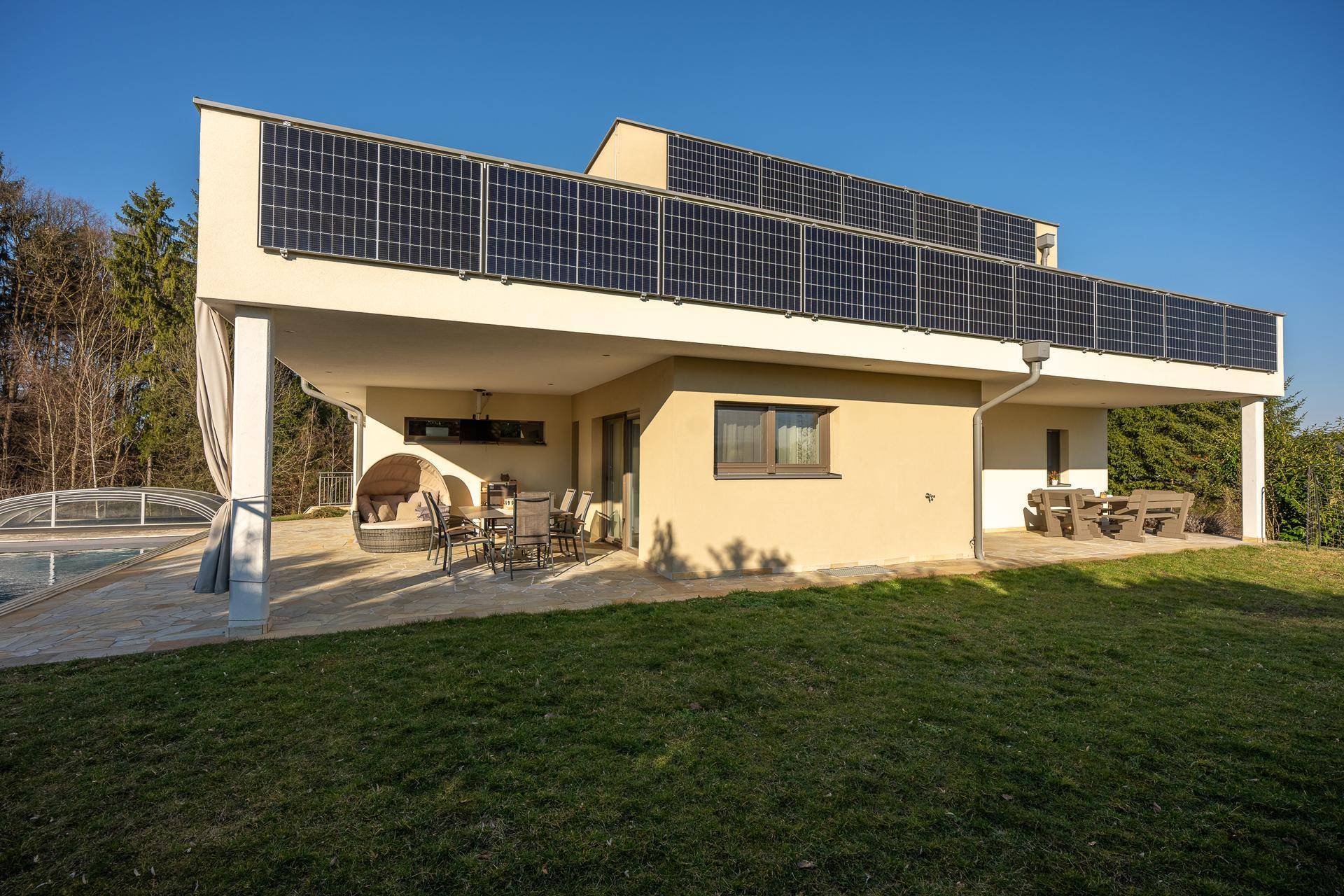 Große überdachte Terrasse mit Sitzgelegenheiten und Photovoltaikanlage auf dem Dach.
