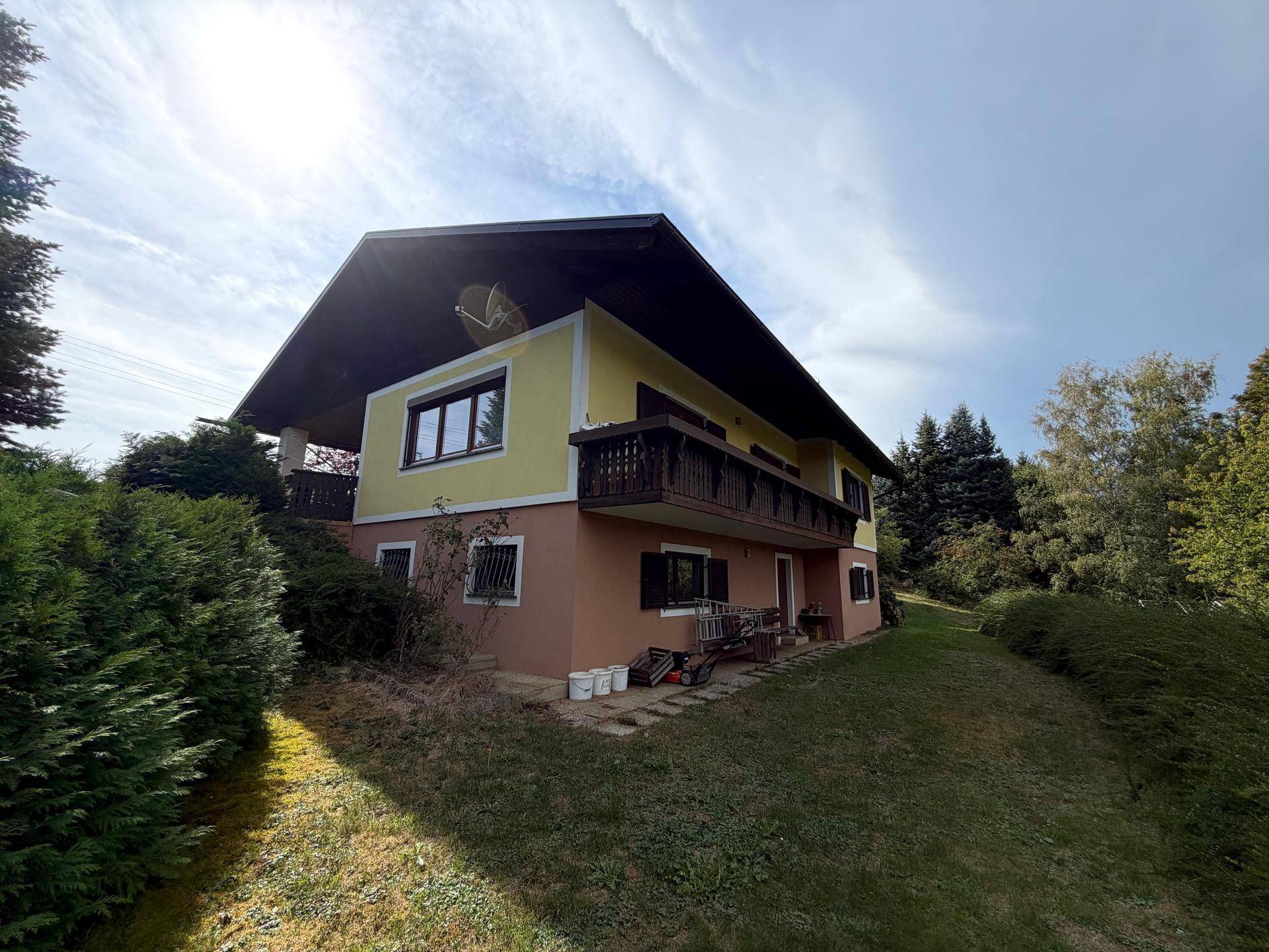 Seitenansicht des Hauses mit Balkon und umgebender grüner Landschaft.