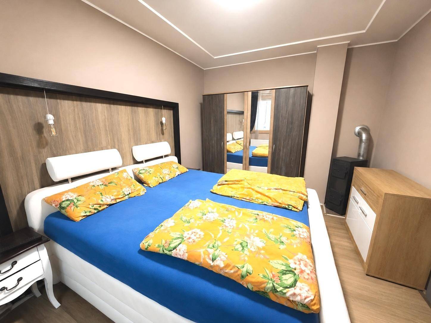 Schlafzimmer mit großem Bett, Spiegelschrank und einem sichtbaren Ofenrohr.