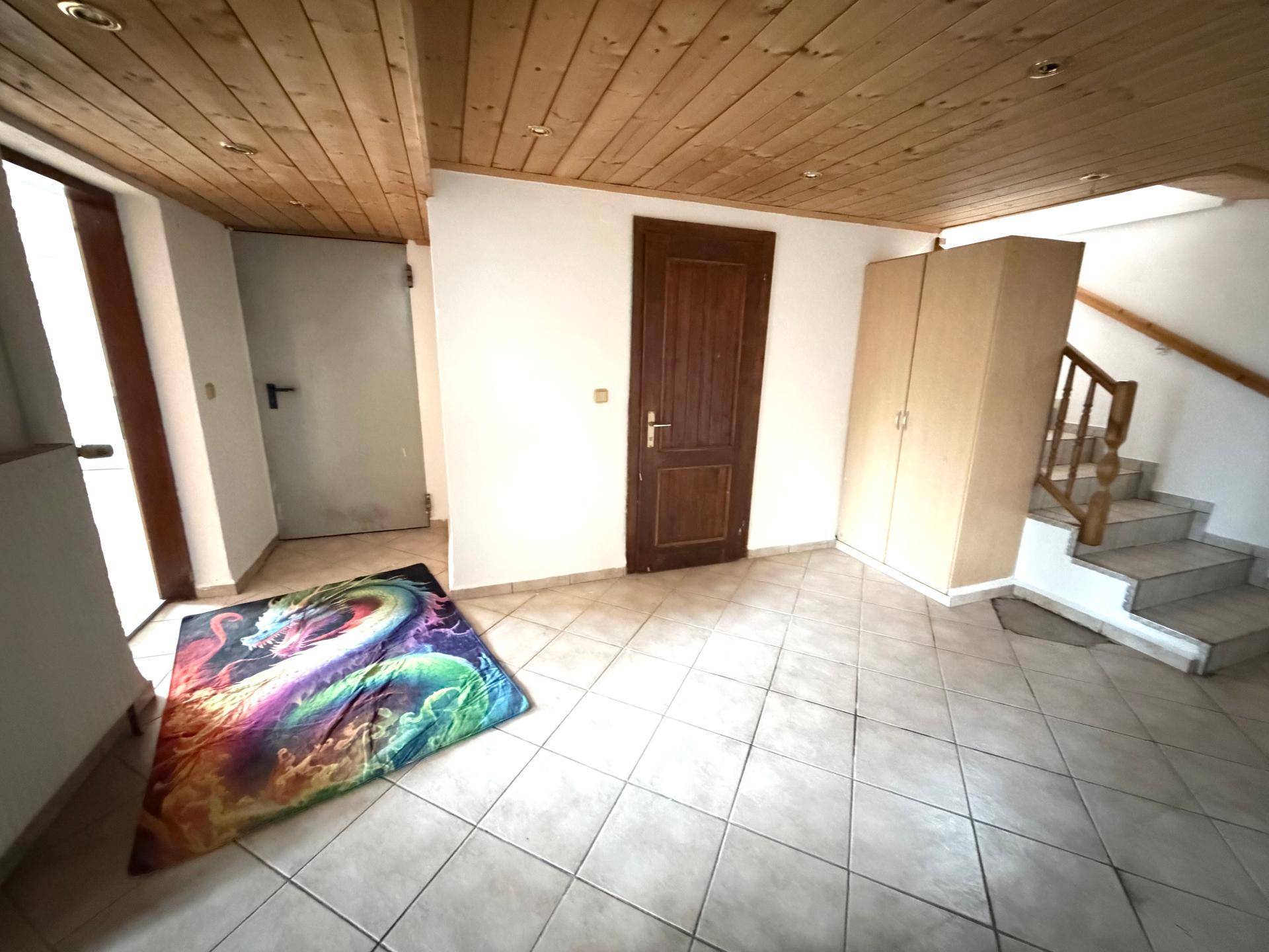 Eingangsbereich mit Fliesenboden, Holzdecke und einem bunten Teppich vor der Tür.