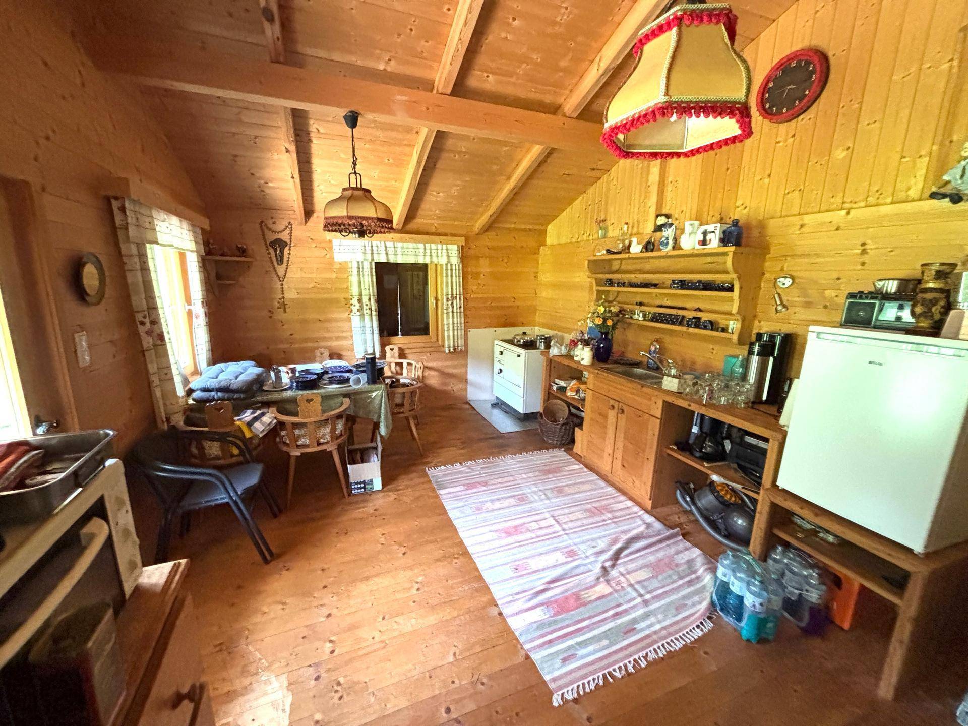 Rustikaler Innenraum einer Holzhütte mit sichtbaren Balken, Holzwänden und einfacher Einrichtung.