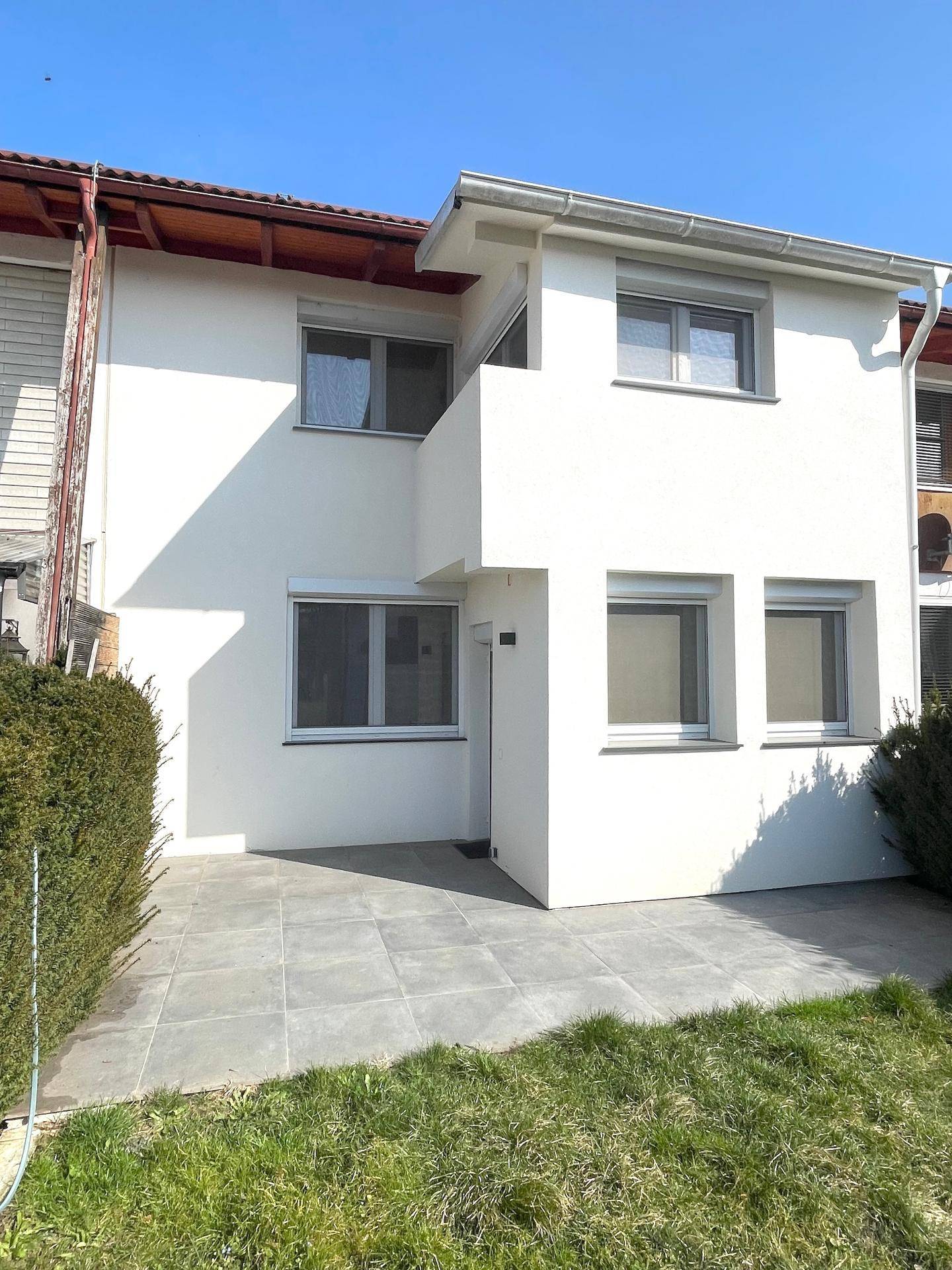 Rückansicht des Hauses mit weißer Fassade, Terrasse und Gartenbereich.