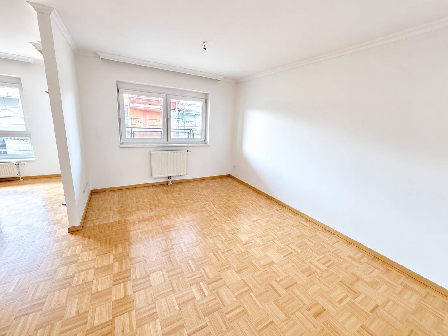 Heller, leerer Wohnraum mit klassischem Parkettboden und weißen Wänden, bereit zur individuellen Gestaltung.