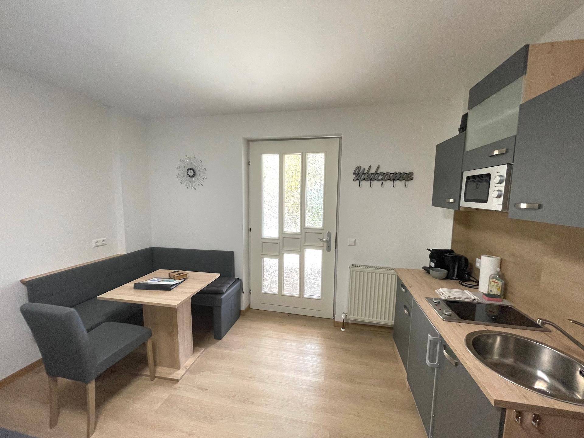 Eine kompakte Küchenzeile mit Essecke und grauen Schränken nahe dem Eingangsbereich.