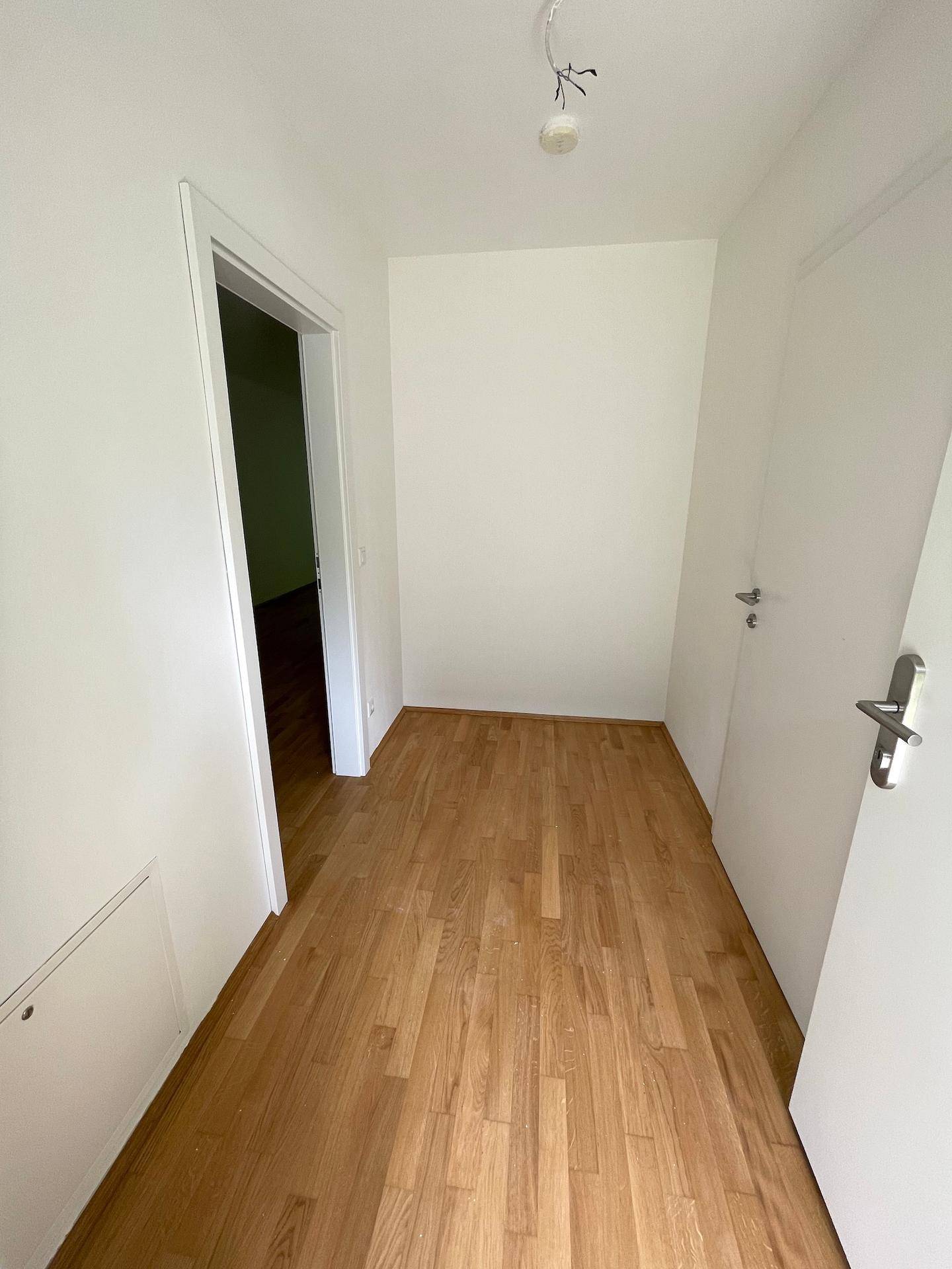 Heller Flur mit Holzboden und weißen Wänden, der zu weiteren Räumen führt.