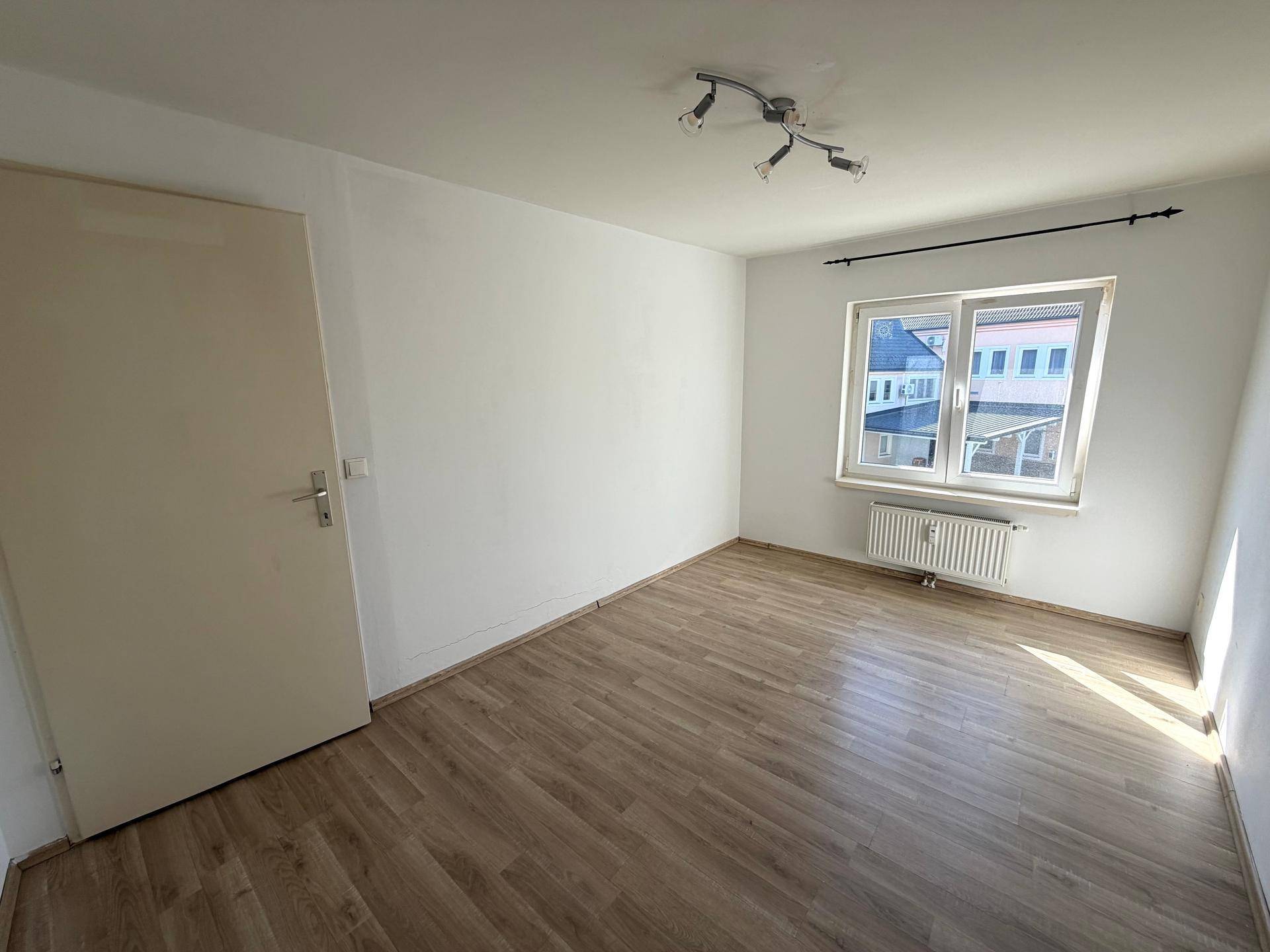 Geräumiges Zimmer mit Laminatboden, weißen Wänden und einem Fenster mit Stadtblick.