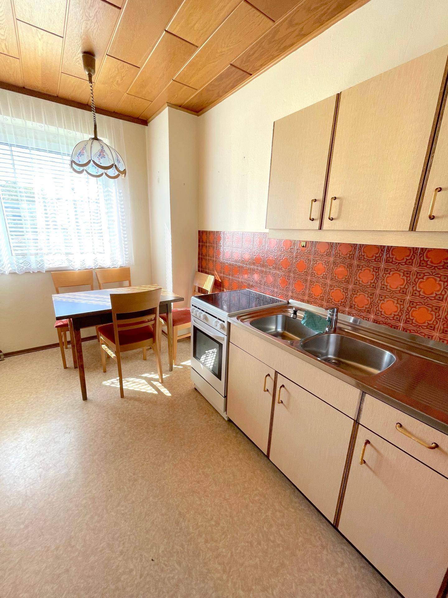 Küche mit Esstisch, Spüle und Herd, charakteristisch für ältere Baujahre.