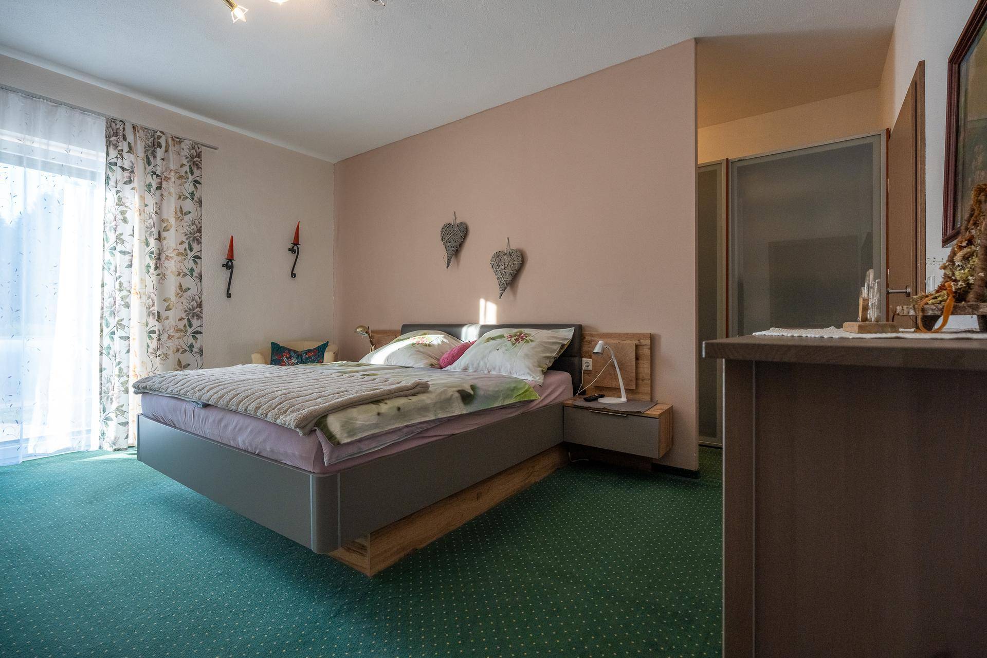 Helles Schlafzimmer mit Doppelbett, Teppichboden und Zugang zu einem Balkon.
