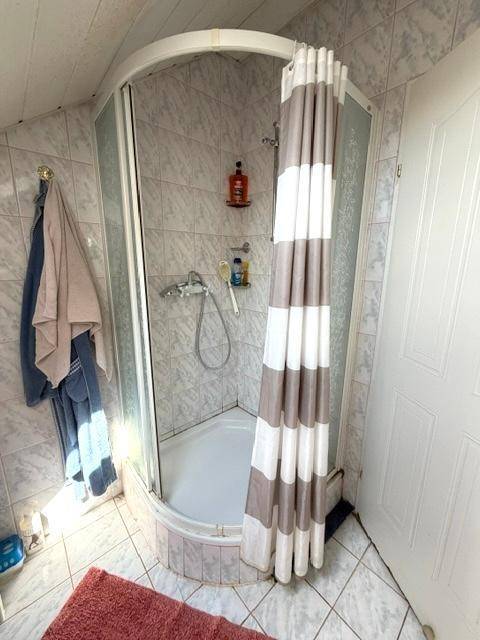 Eckdusche mit gestreiftem Vorhang in einem gefliesten Badezimmer mit Dachschräge.