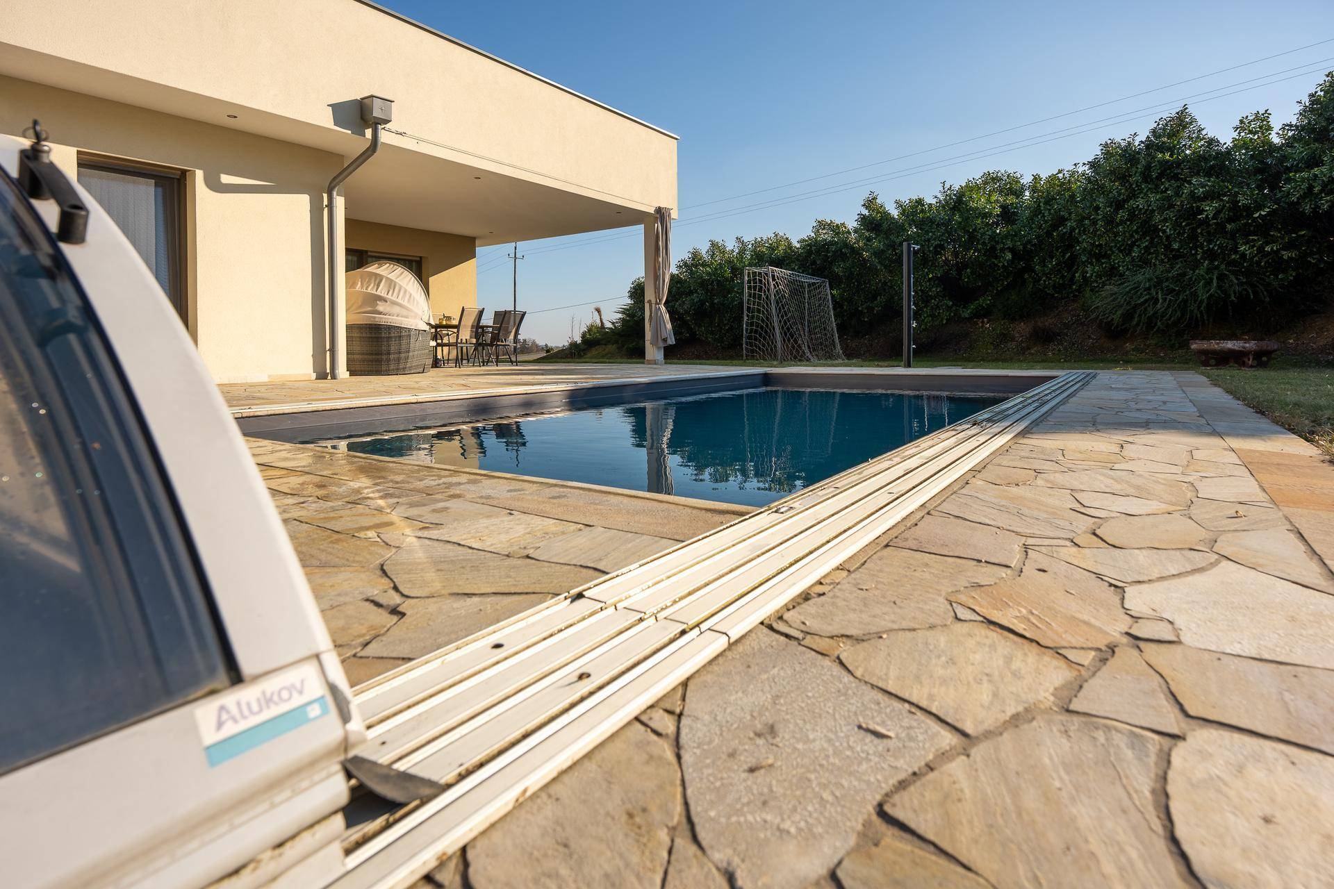 Außenbereich mit Swimmingpool, Steinfliesen und einer überdachten Terrasse im Hintergrund.