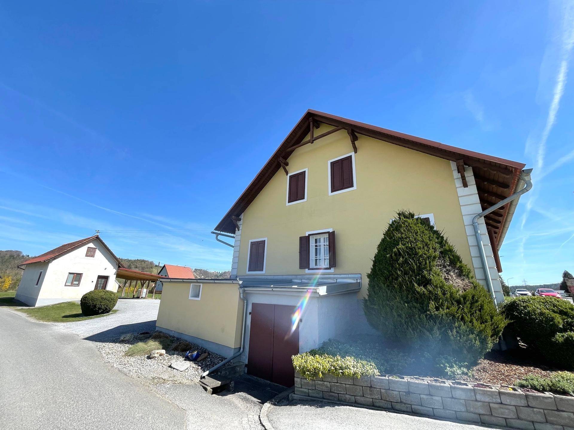 Seitenansicht des Hauses mit gelber Fassade, roten Fensterläden und einem Garagentor im Untergeschoss.