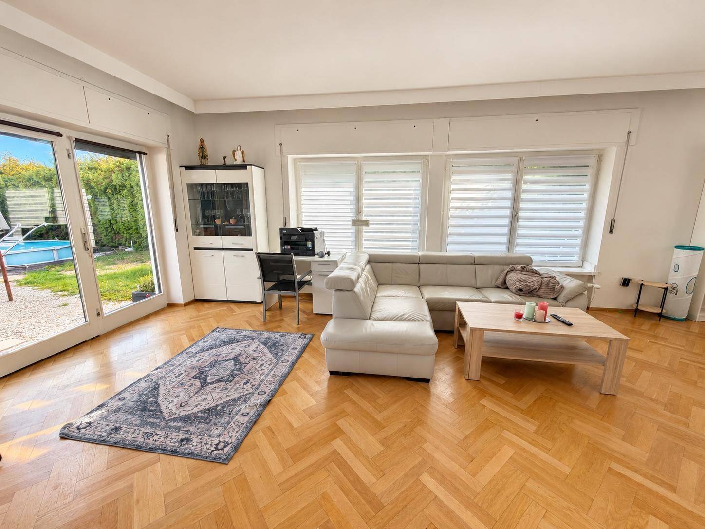 Gemütliches Wohnzimmer mit Fischgrätparkett, Sofa und großen Fenstern mit Zugang zum Garten und Pool.