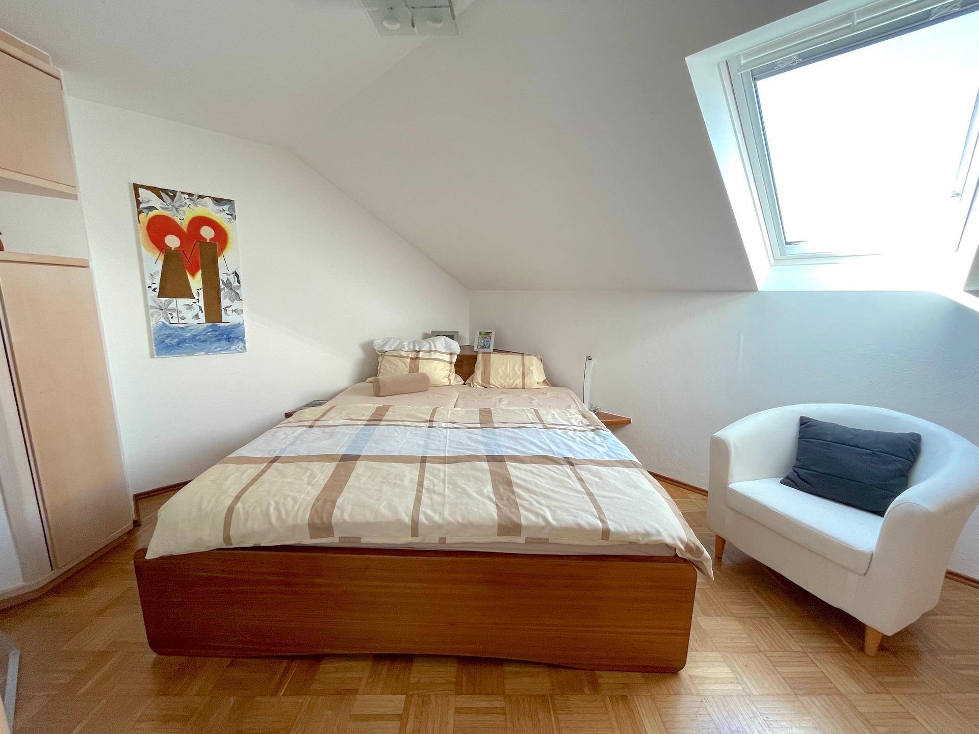 Gemütliches Schlafzimmer im Dachgeschoss mit Holzbett, Sessel und Dachfenster für viel Licht.
