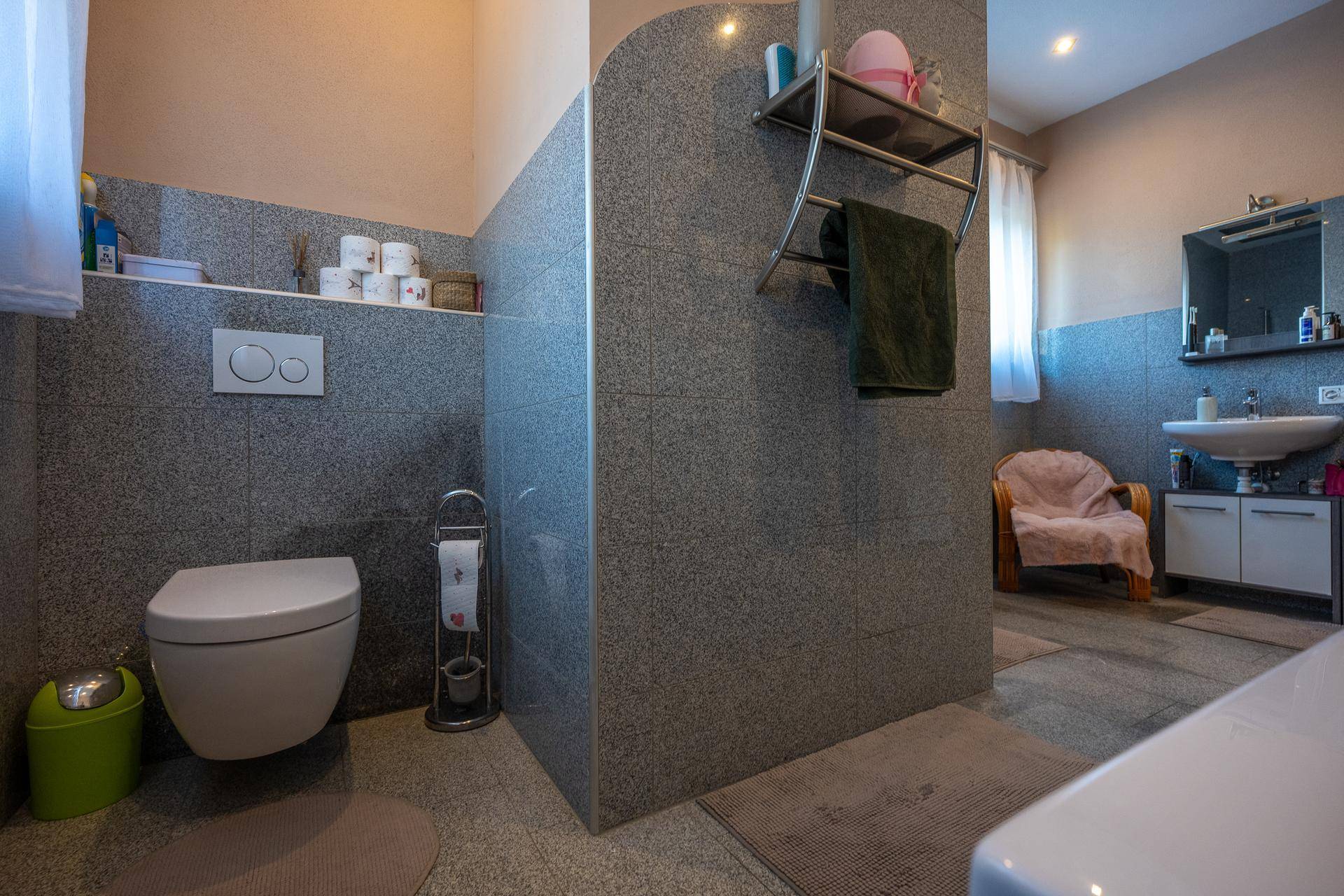 Badezimmer mit WC, Waschbecken, Dusche und großem Spiegel, hell gefliest.