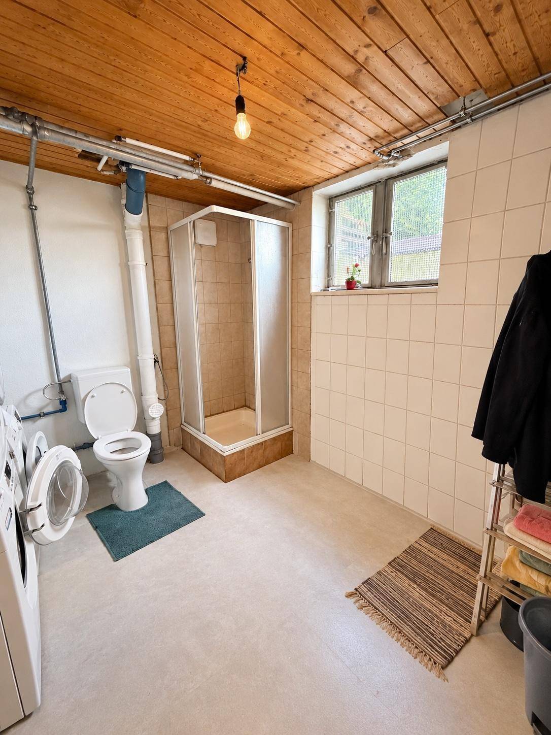 Funktionaler Waschraum im Keller mit Duschkabine, Toilette und Waschmaschinen.