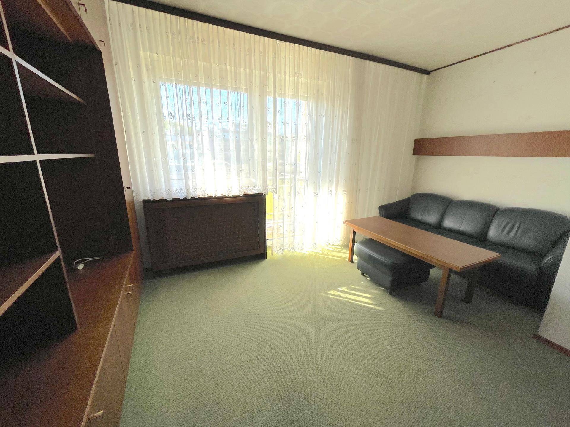 Helles Wohnzimmer mit Sofa, Couchtisch und großem Fenster, ausgestattet mit Teppichboden.