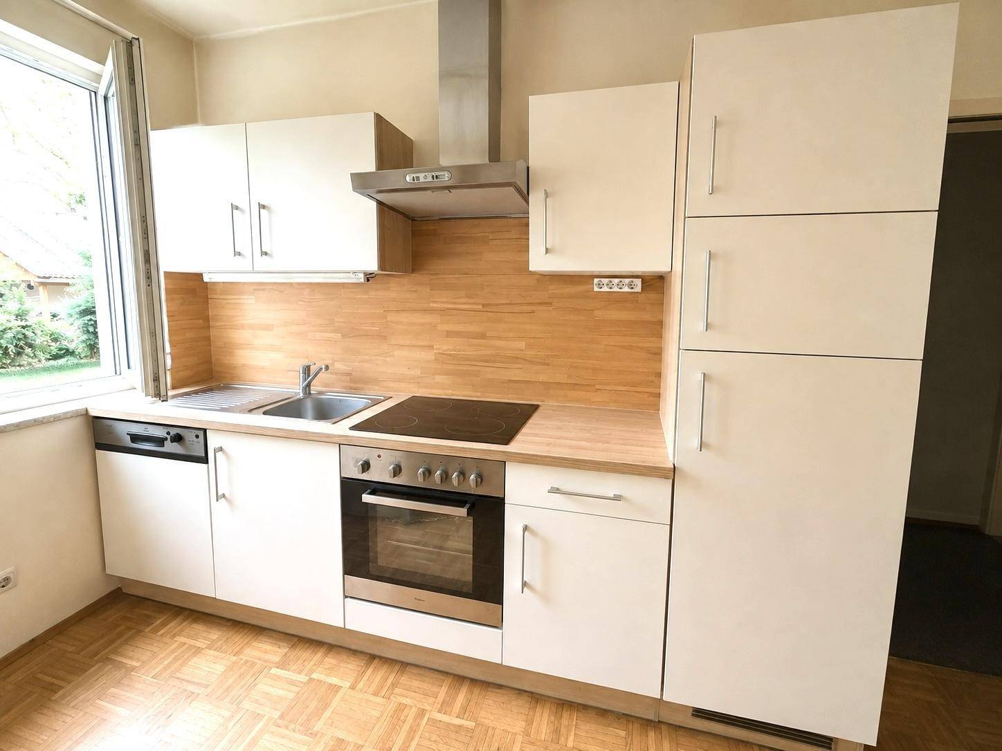Moderne Einbauküche mit weißen Schränken, Holzoptik-Arbeitsplatte und integrierten Geräten.