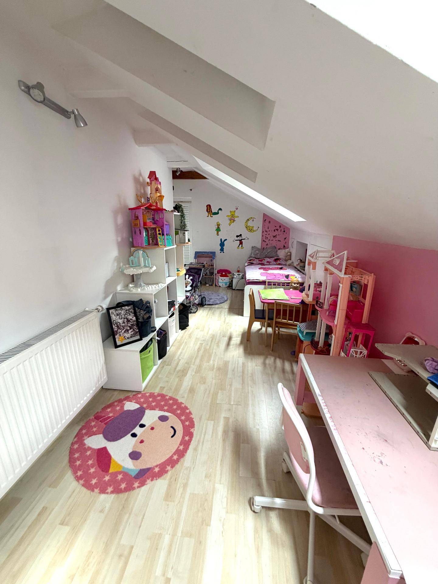 Kinderzimmer unter der Dachschräge mit Spielbereich und rosa Wänden.