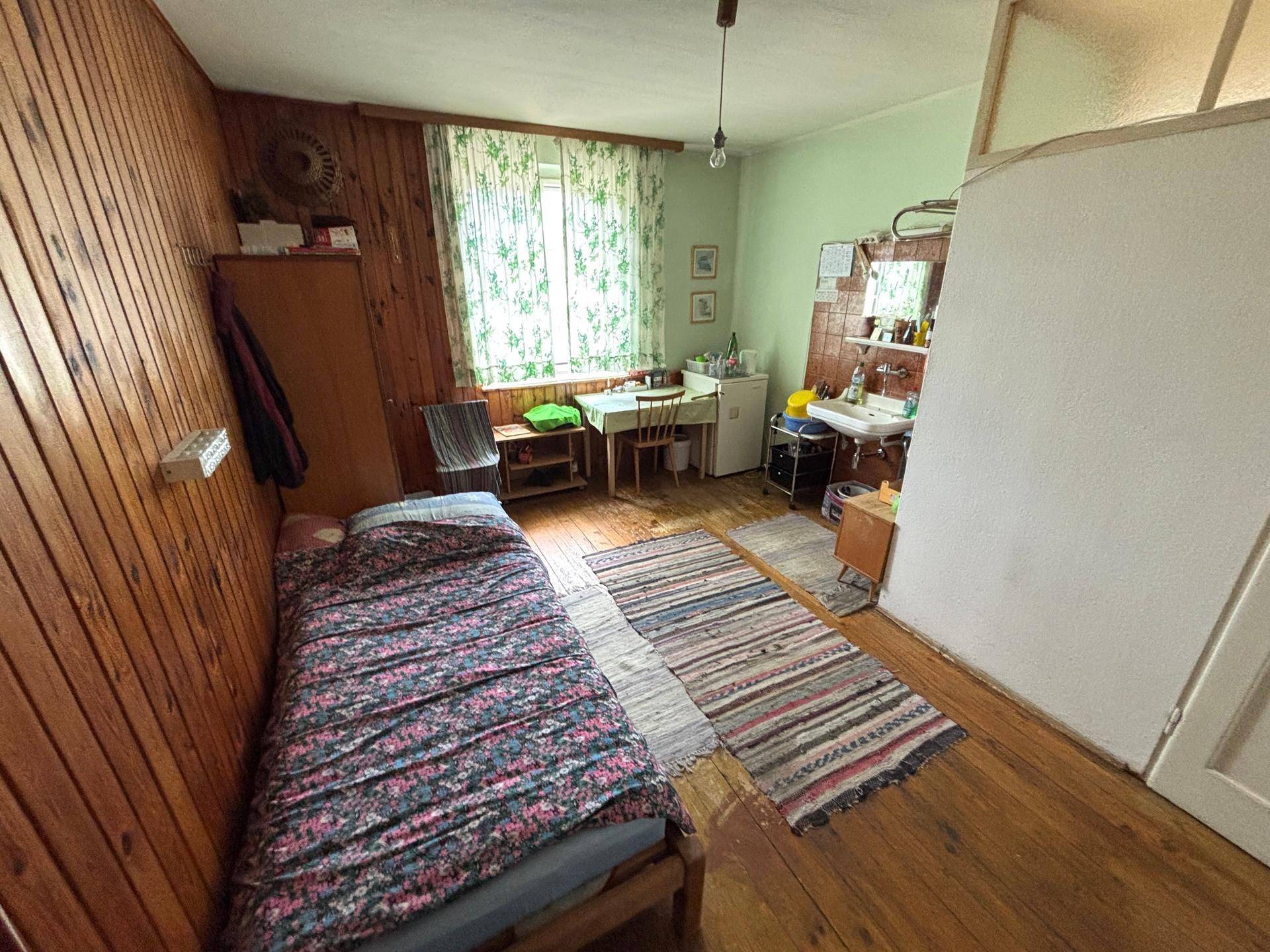 Schlafzimmer mit Holzwänden, Holzboden und Einzelbett, hell durch Fenster.