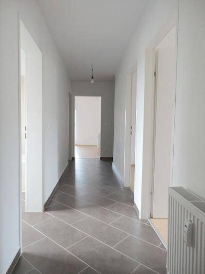 Langer Flur mit diagonal verlegten Fliesen und Zugang zu verschiedenen Räumen.