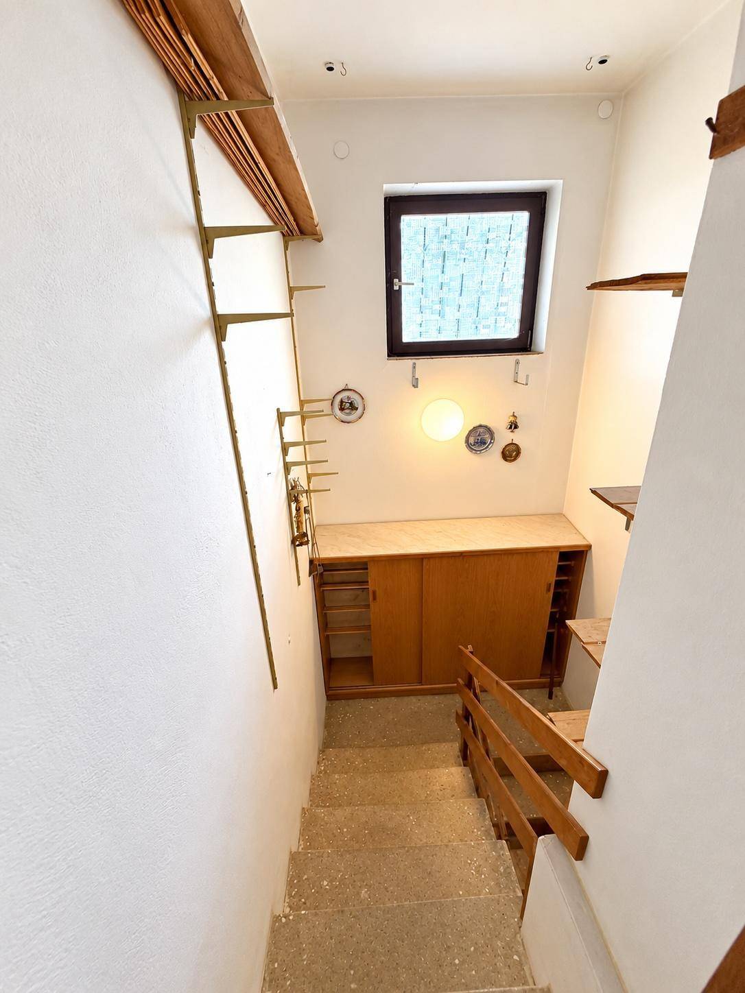 Treppenhaus mit Holzgeländer, Fenster und Stauraum unter der Treppe.