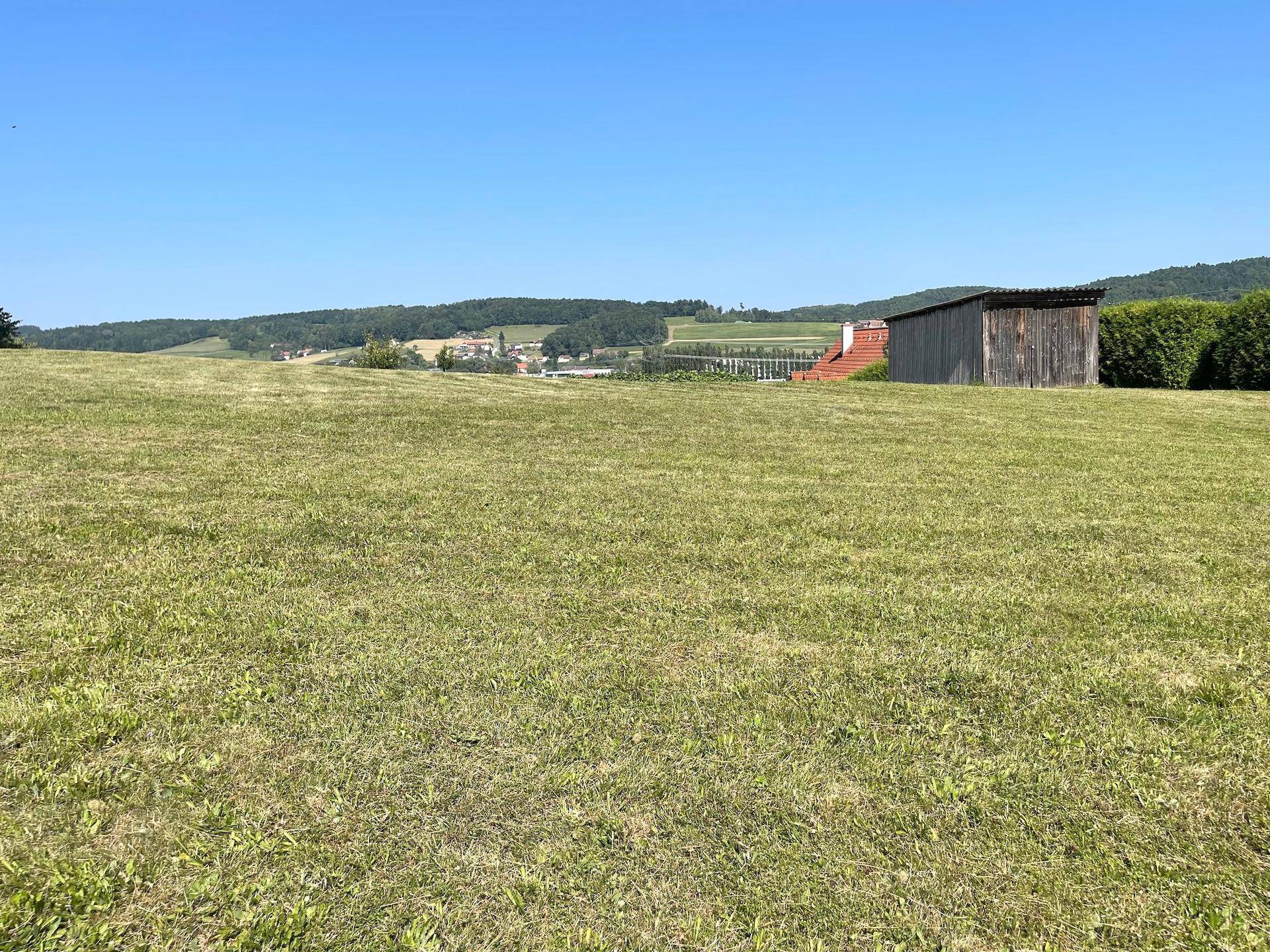 Weitläufige Rasenfläche mit einem Holzschuppen und Panoramablick auf die ländliche Umgebung und entfernte Häuser.