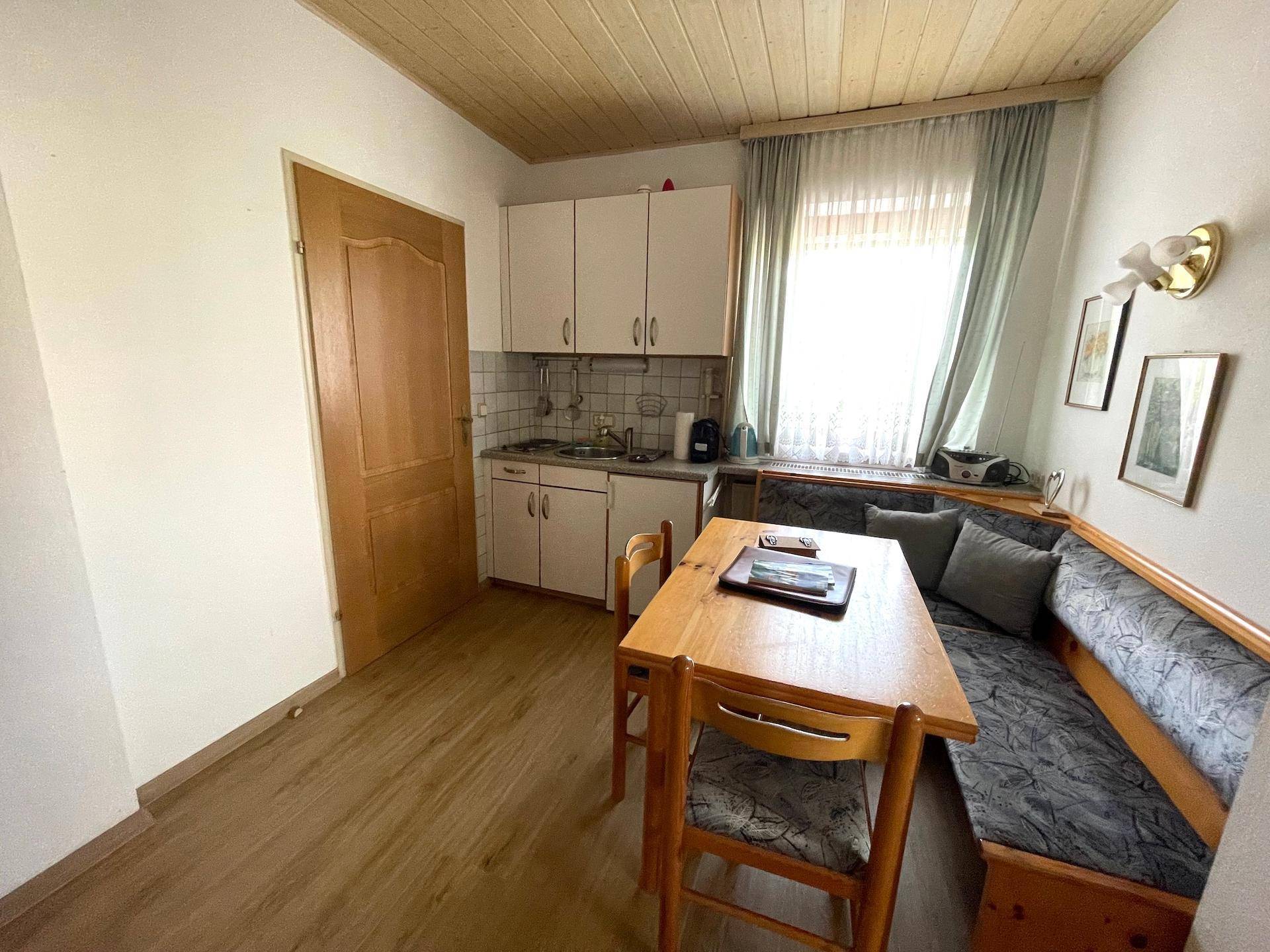 Eine kleine Küchenzeile mit Essbereich und hellem Laminatboden unter einer Holzdecke.